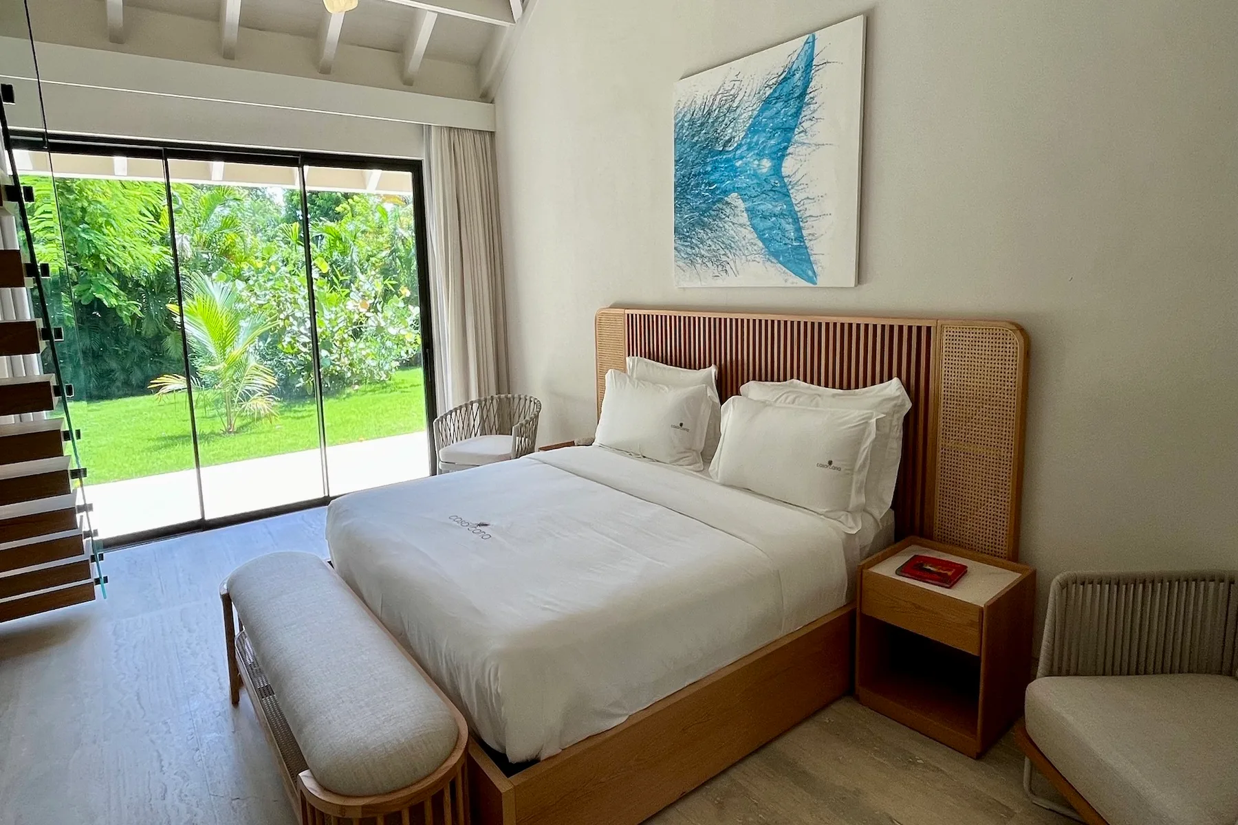 Un dormitorio luminoso con una cama tendida y puertas corredizas de vidrio hacia la vegetación.
