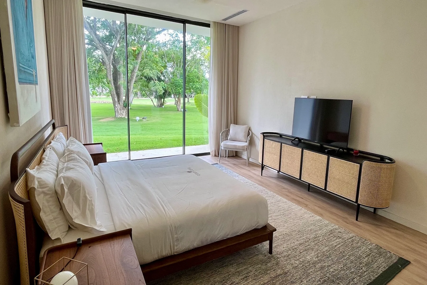 Un dormitorio con una cama junto a grandes ventanales que dan a un césped verde.