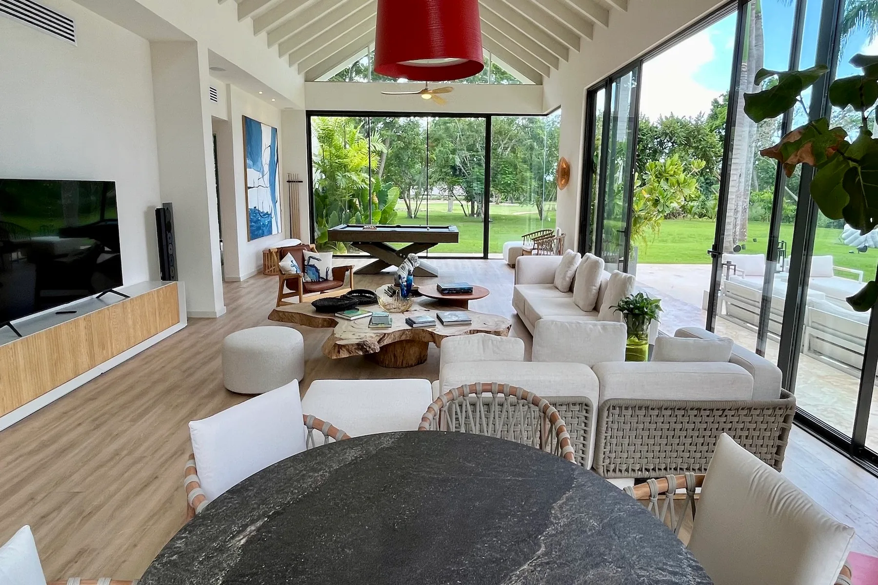 Una sala luminosa con asientos, un televisor y grandes ventanas con vistas a zonas verdes.