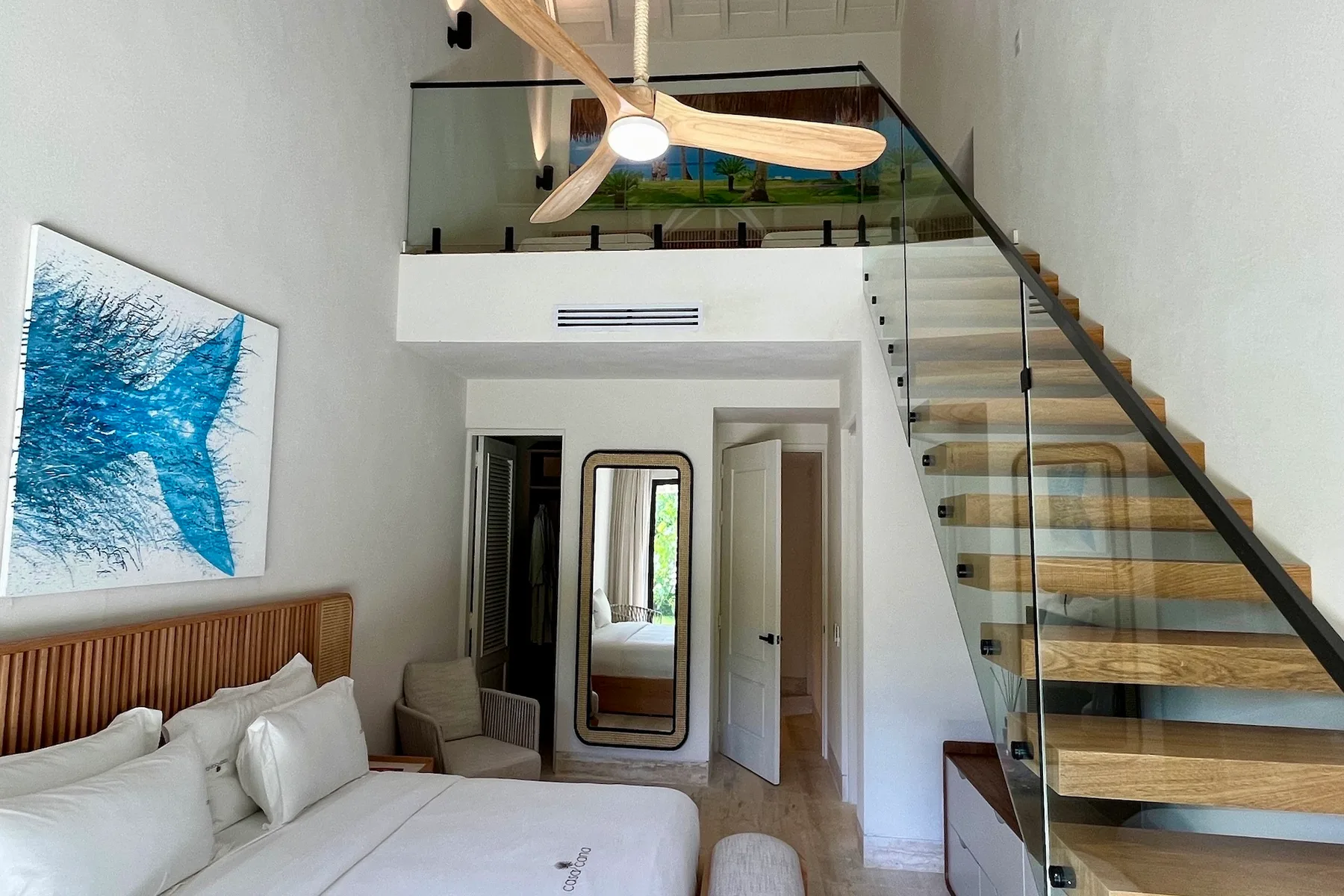 Un dormitorio luminoso con una cama, arte en la pared y una escalera hacia un nivel superior.