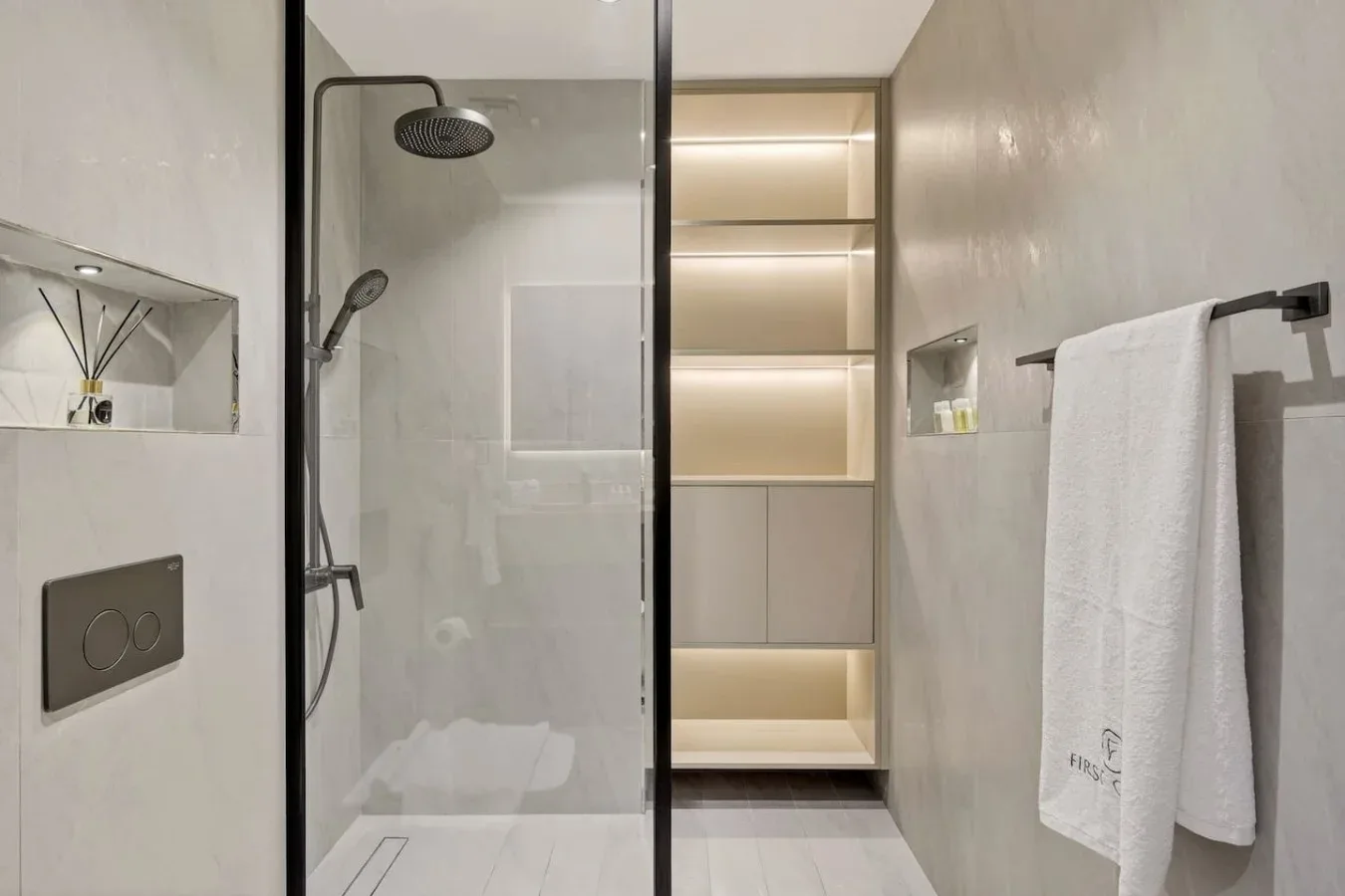A bright bathroom with a glass shower and illuminated recessed shelves.