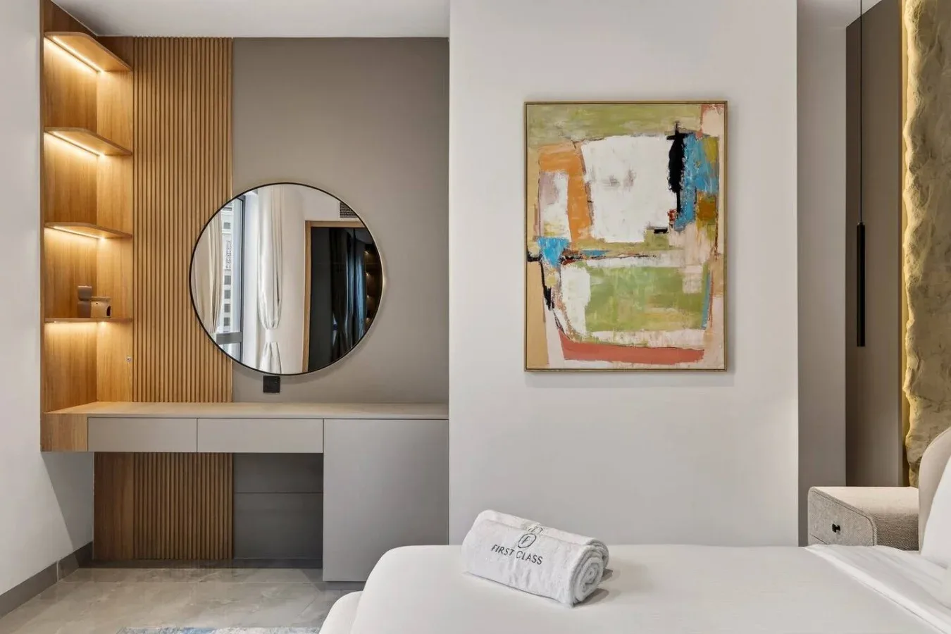 A bedroom vanity with a round mirror, illuminated shelves, and abstract wall art.