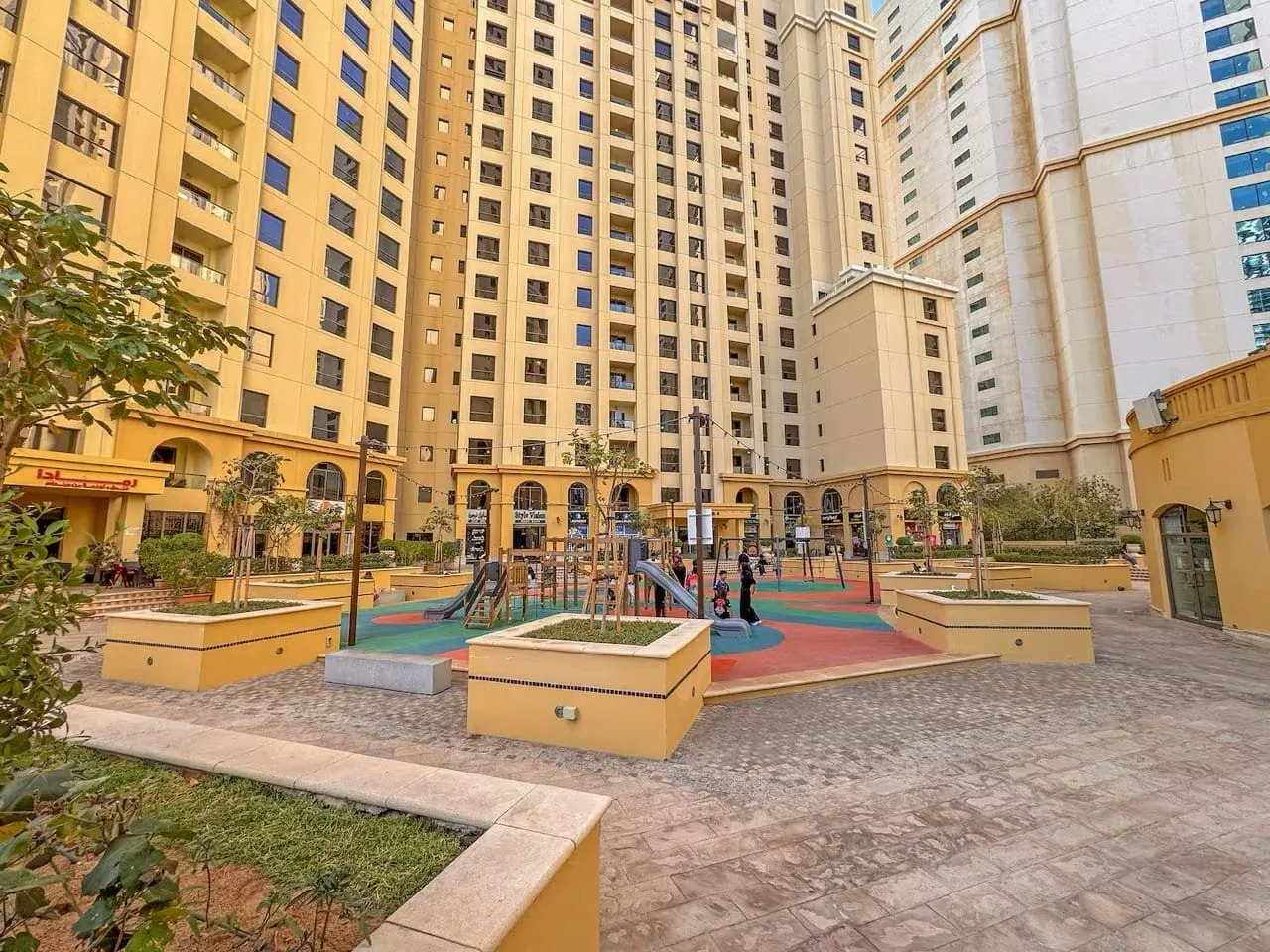 A paved courtyard with a colorful playground between tall apartment buildings.