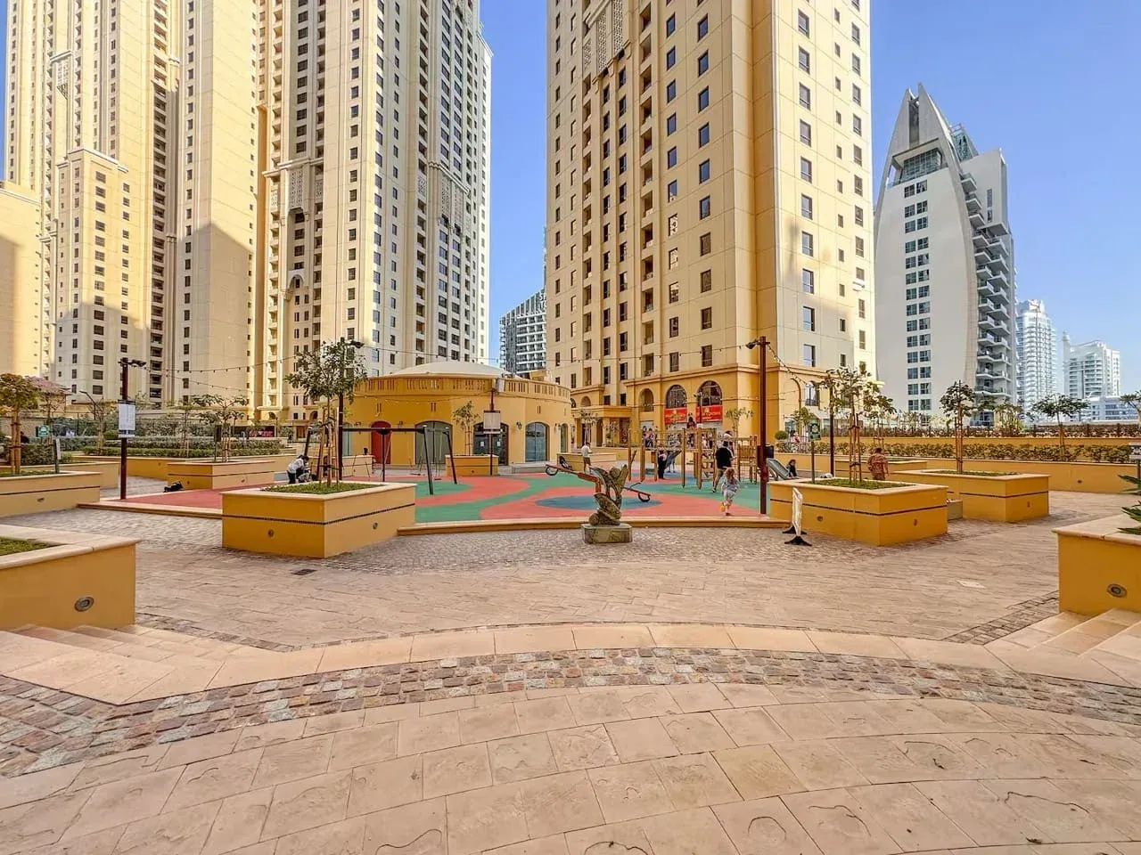 A paved courtyard with colorful play areas sits among tall apartment buildings.
