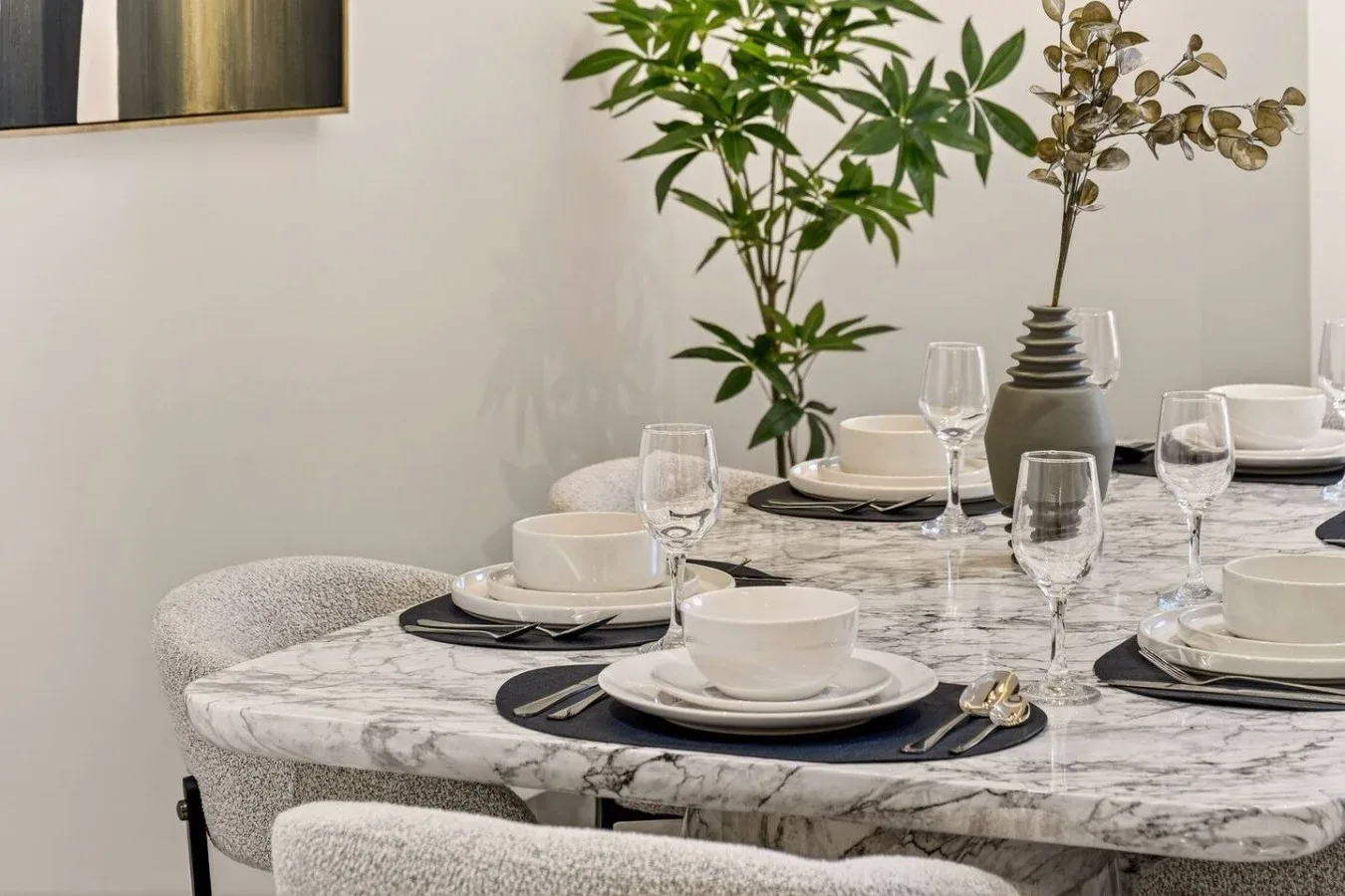A dining table is set with dishes and glassware beside leafy plants.