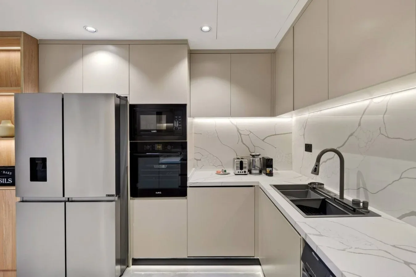 A modern kitchen with pale cabinetry, built-in appliances, and a long countertop.