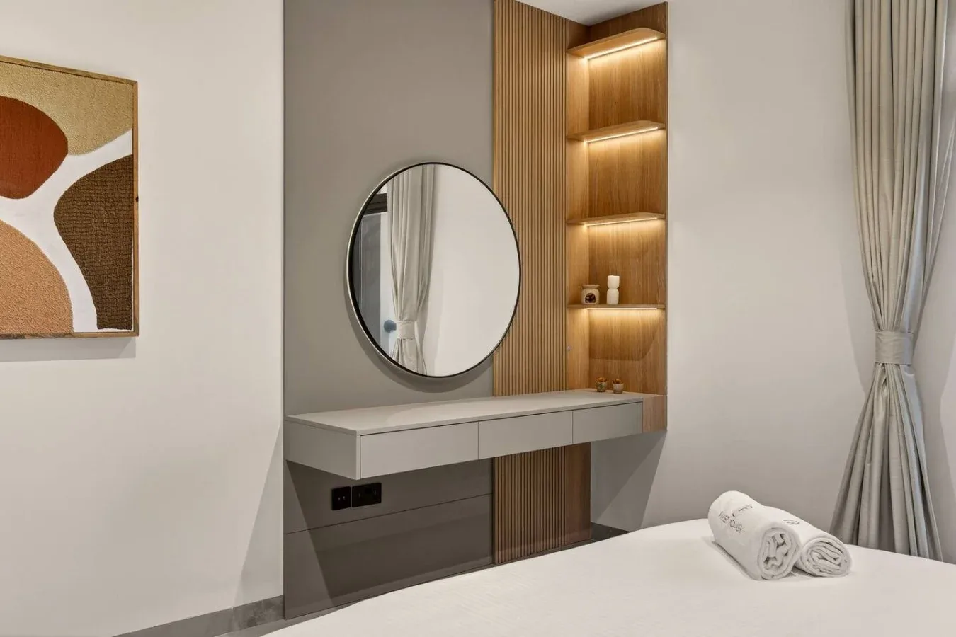 A bedroom vanity with a round mirror and illuminated shelves beside the bed.
