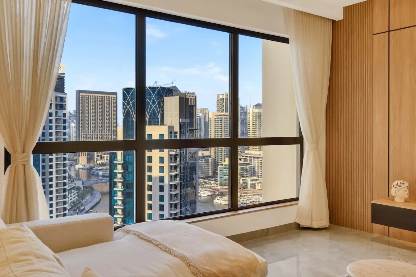 A bedroom with a bed beside a large window overlooking city buildings.