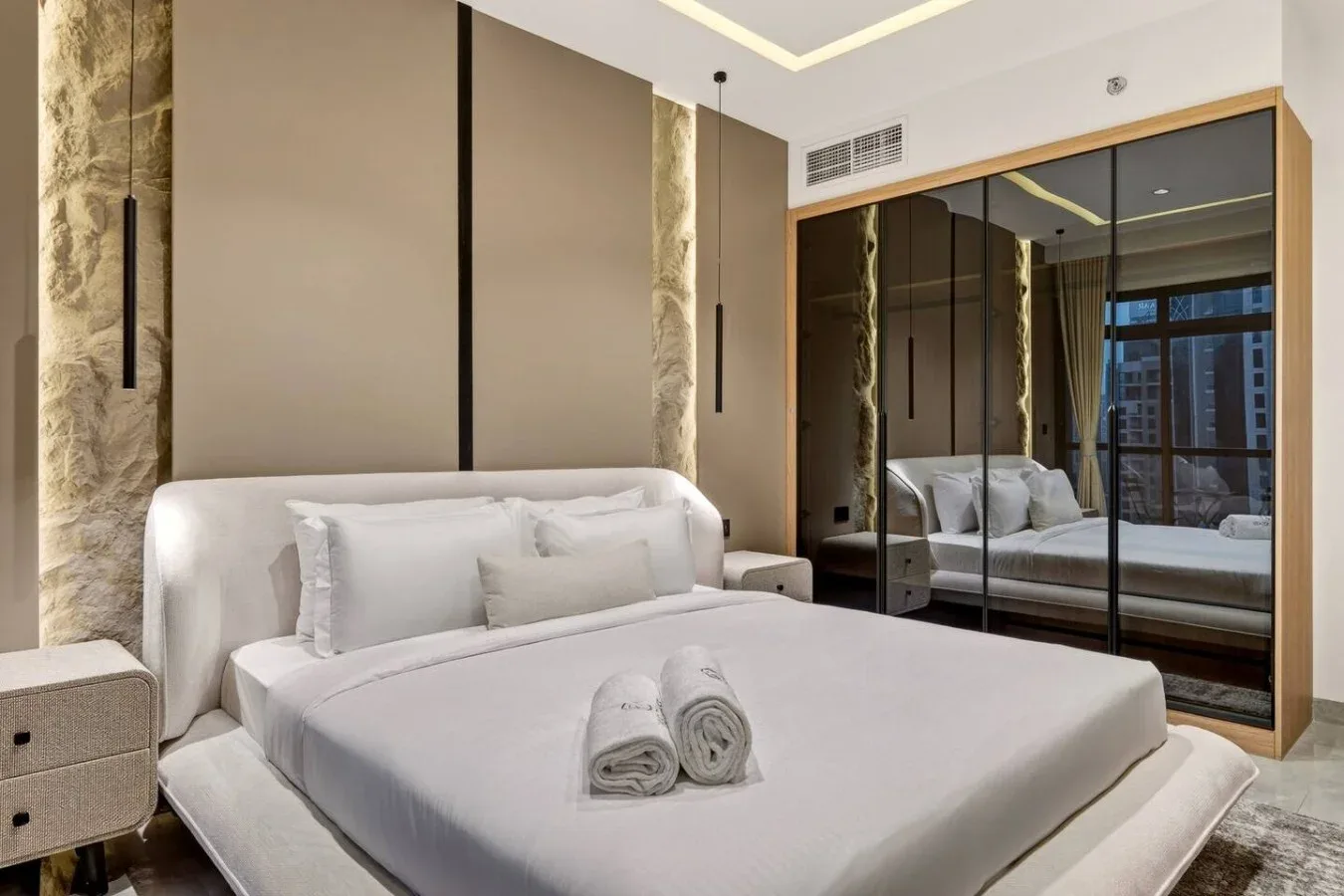A modern bedroom with a neatly made bed and mirrored wardrobe.