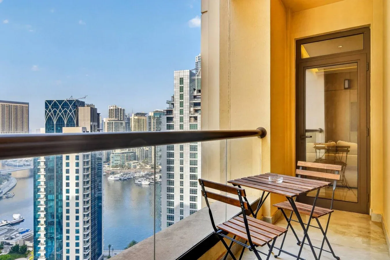 A balcony with a small table and seating overlooks a waterfront city skyline.