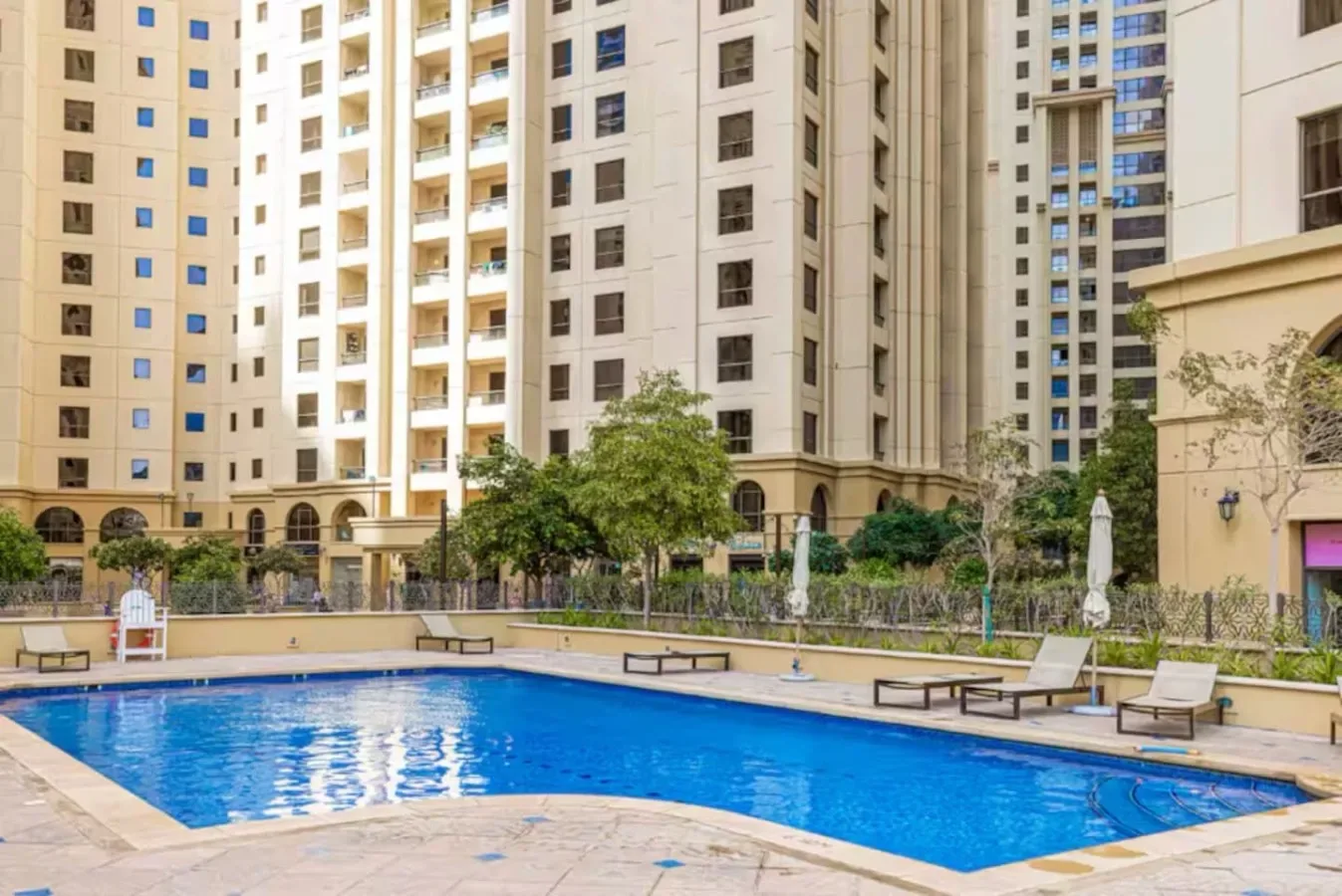 An outdoor swimming pool sits among tall apartment buildings and landscaped grounds.