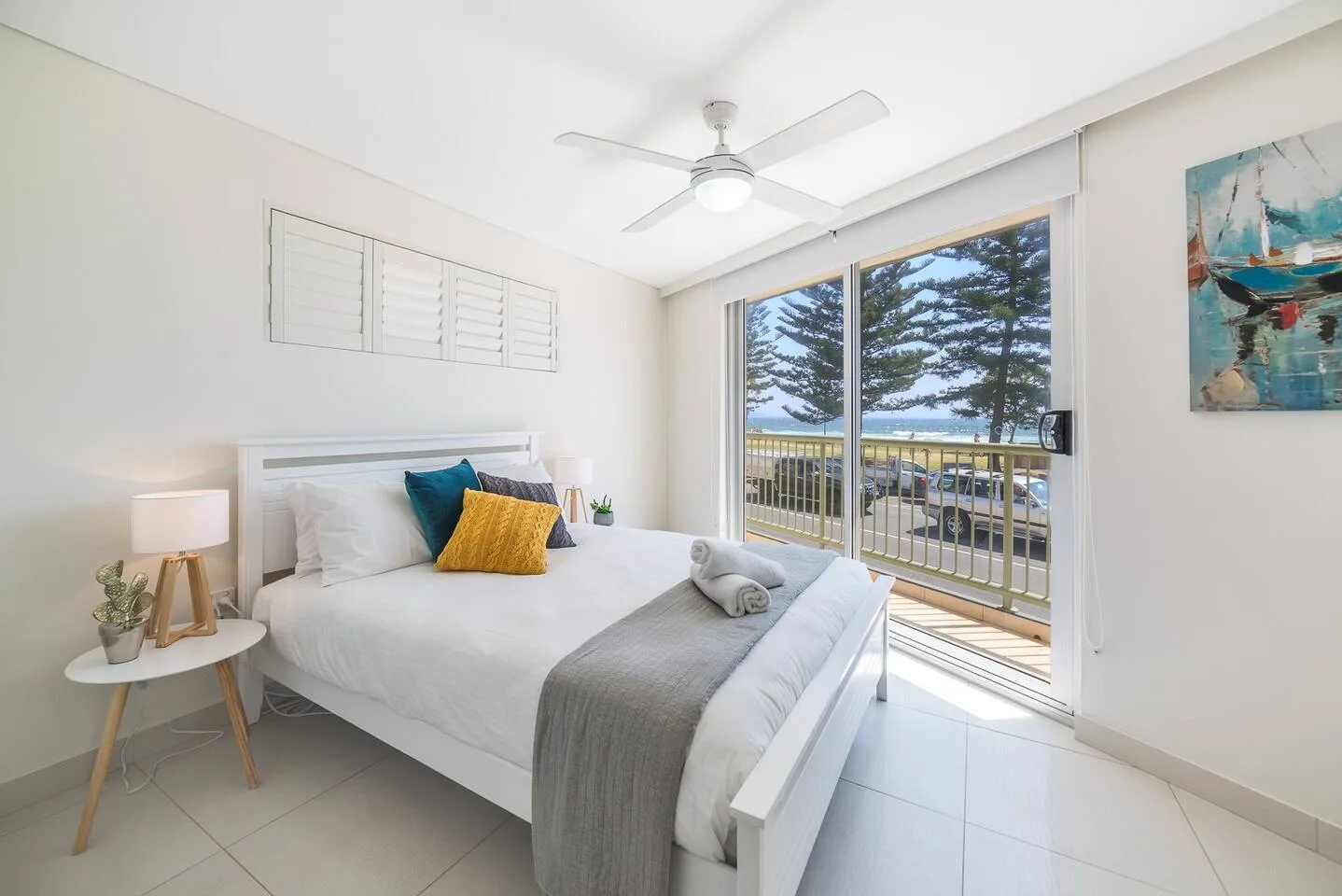 A bright bedroom with a bed beside sliding glass doors opening onto a balcony.