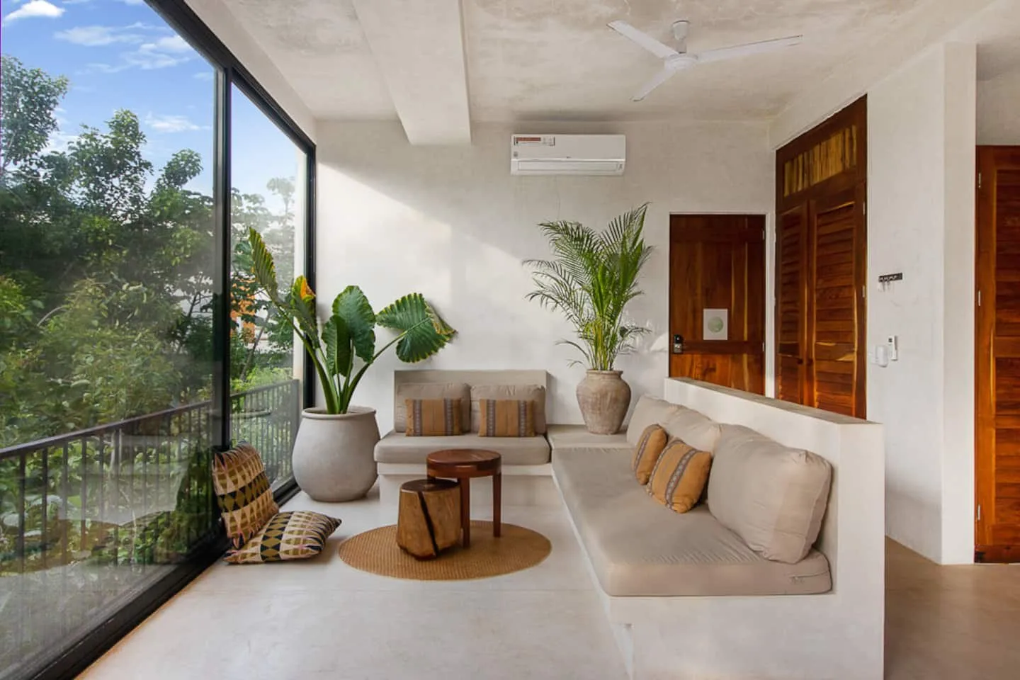 Una luminosa sala de estar con asientos acolchados, plantas en macetas y una gran ventana de vidrio.