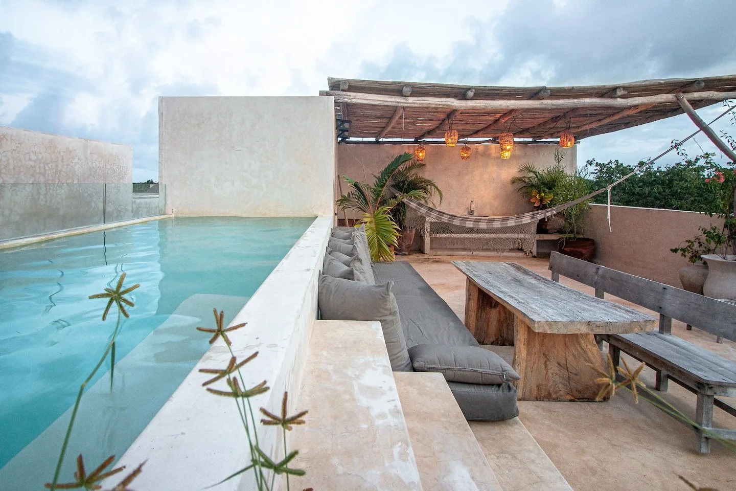 Una piscina exterior y zona de descanso con asientos bajo una pérgola de madera.