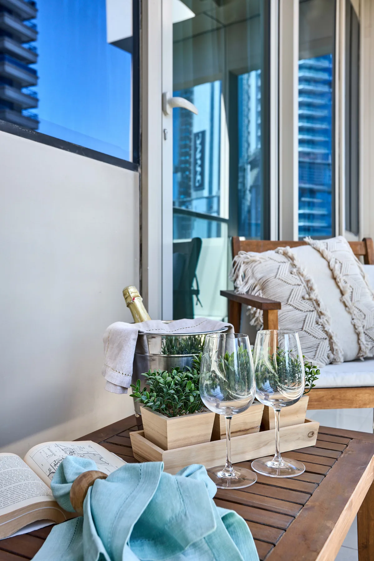 Una zona de estar en el balcón con una mesa de madera y vistas de la ciudad a través del vidrio.