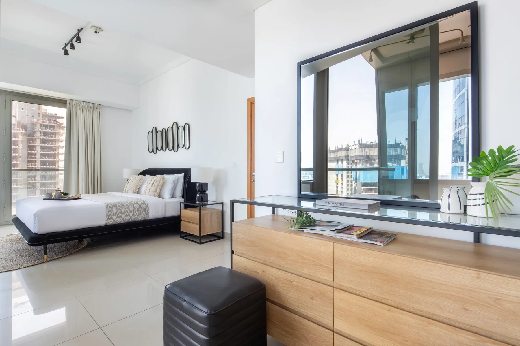 Un dormitorio luminoso con una cama junto a un ventanal con edificios a la vista.
