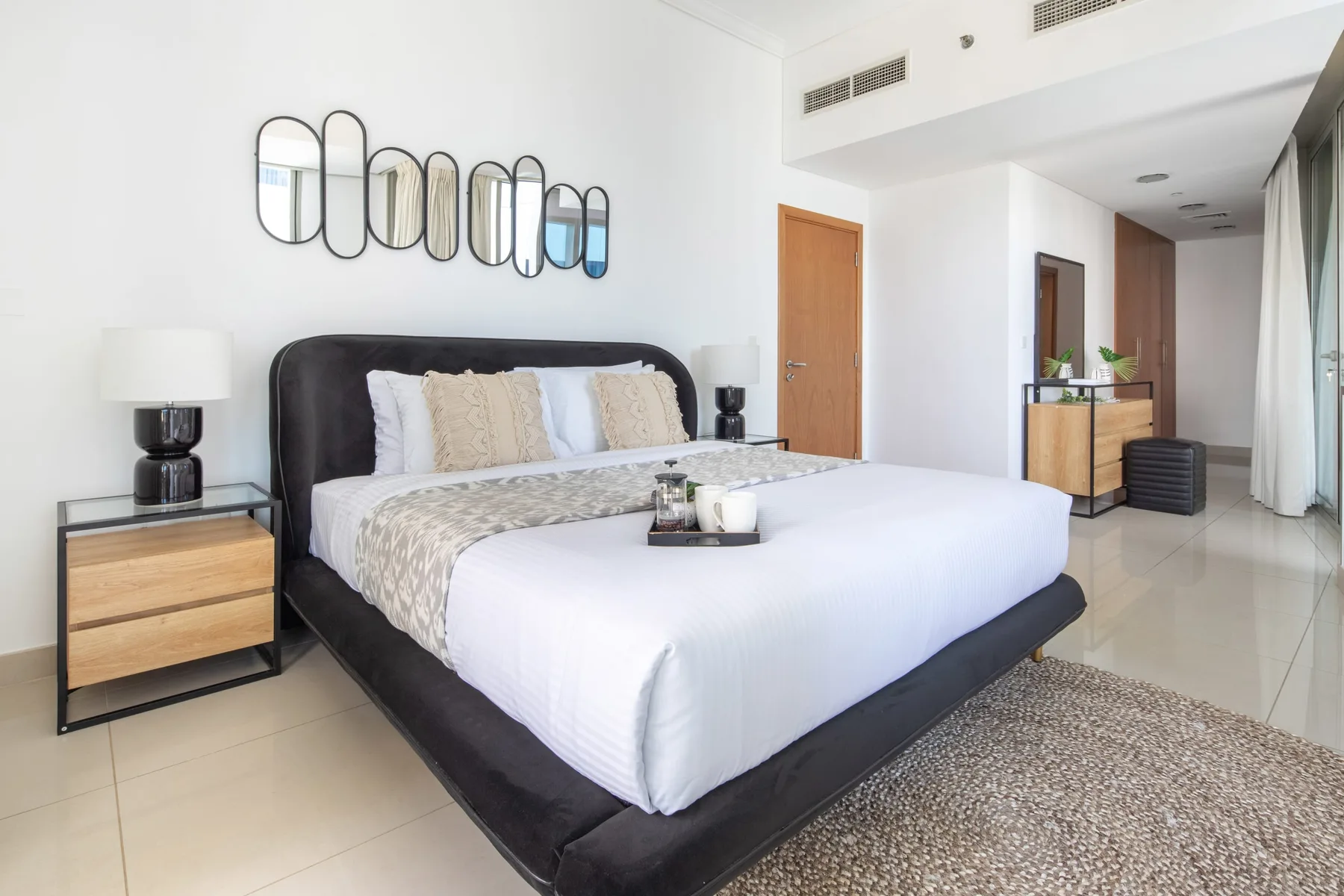 Un dormitorio luminoso con una cama grande, mesitas de noche y espejos sobre el cabecero.