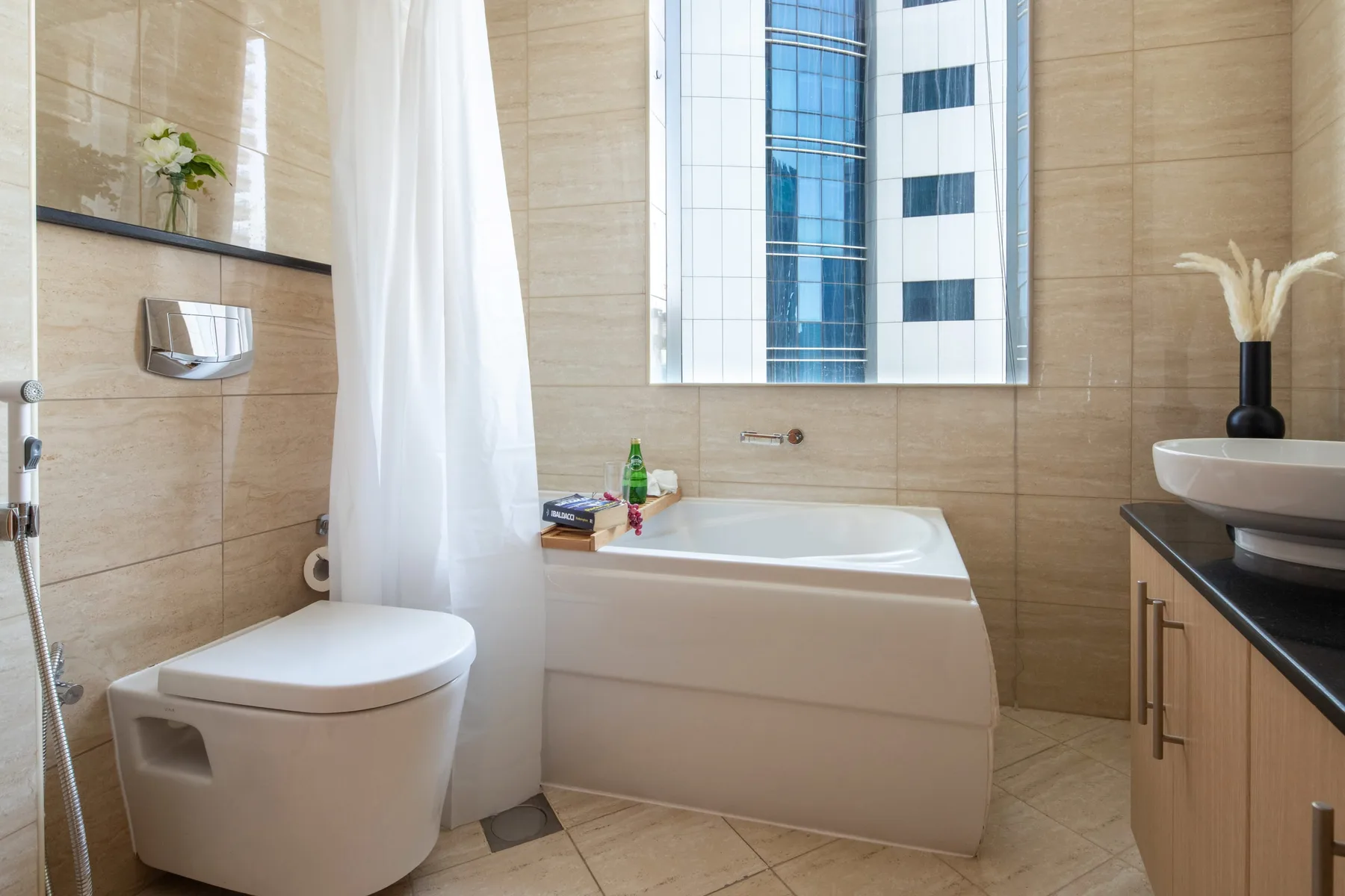 Un baño alicatado con bañera, inodoro y lavabo bajo una ventana grande.