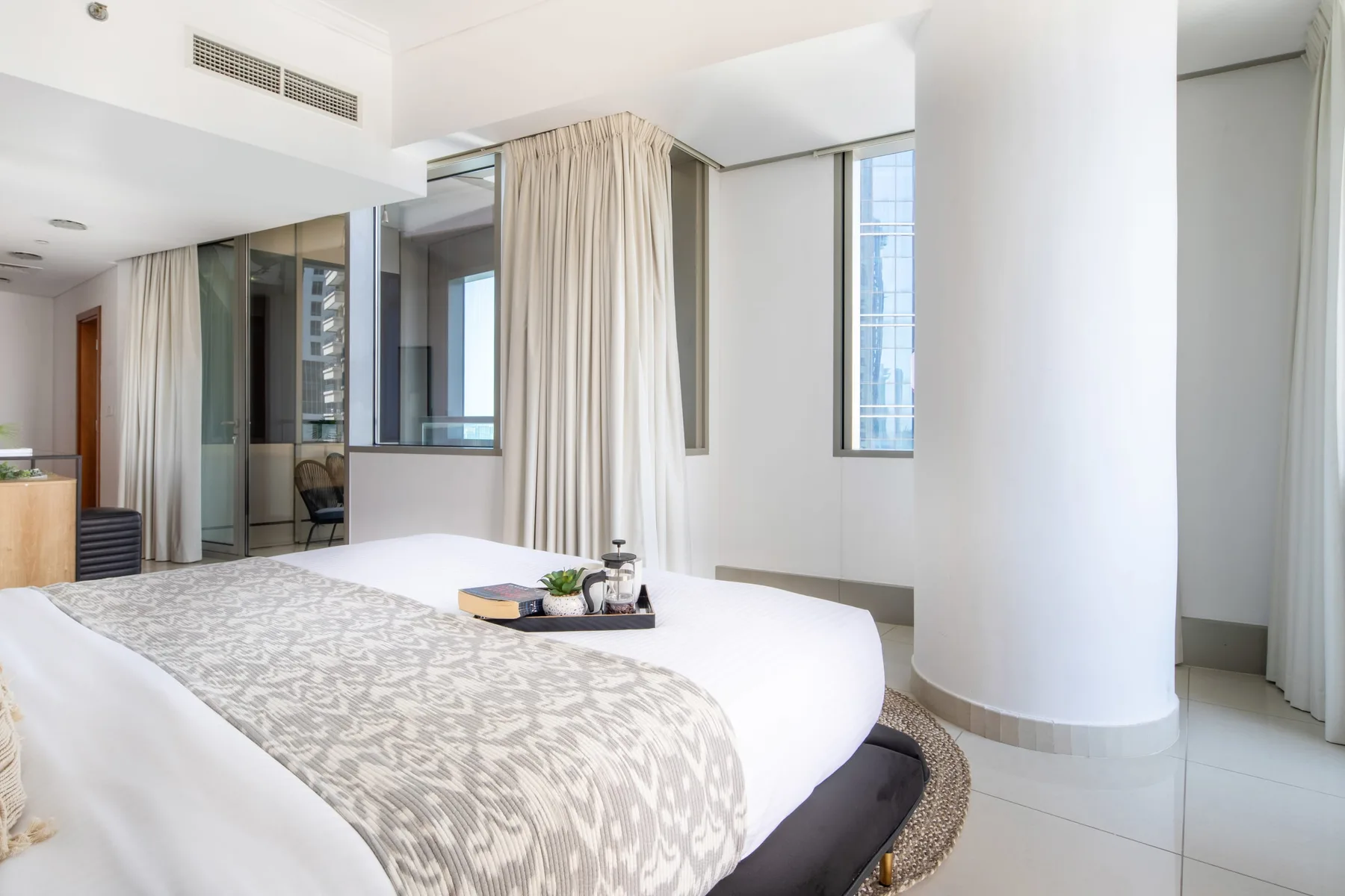 Un dormitorio luminoso con una cama bien arreglada y cortinas largas.