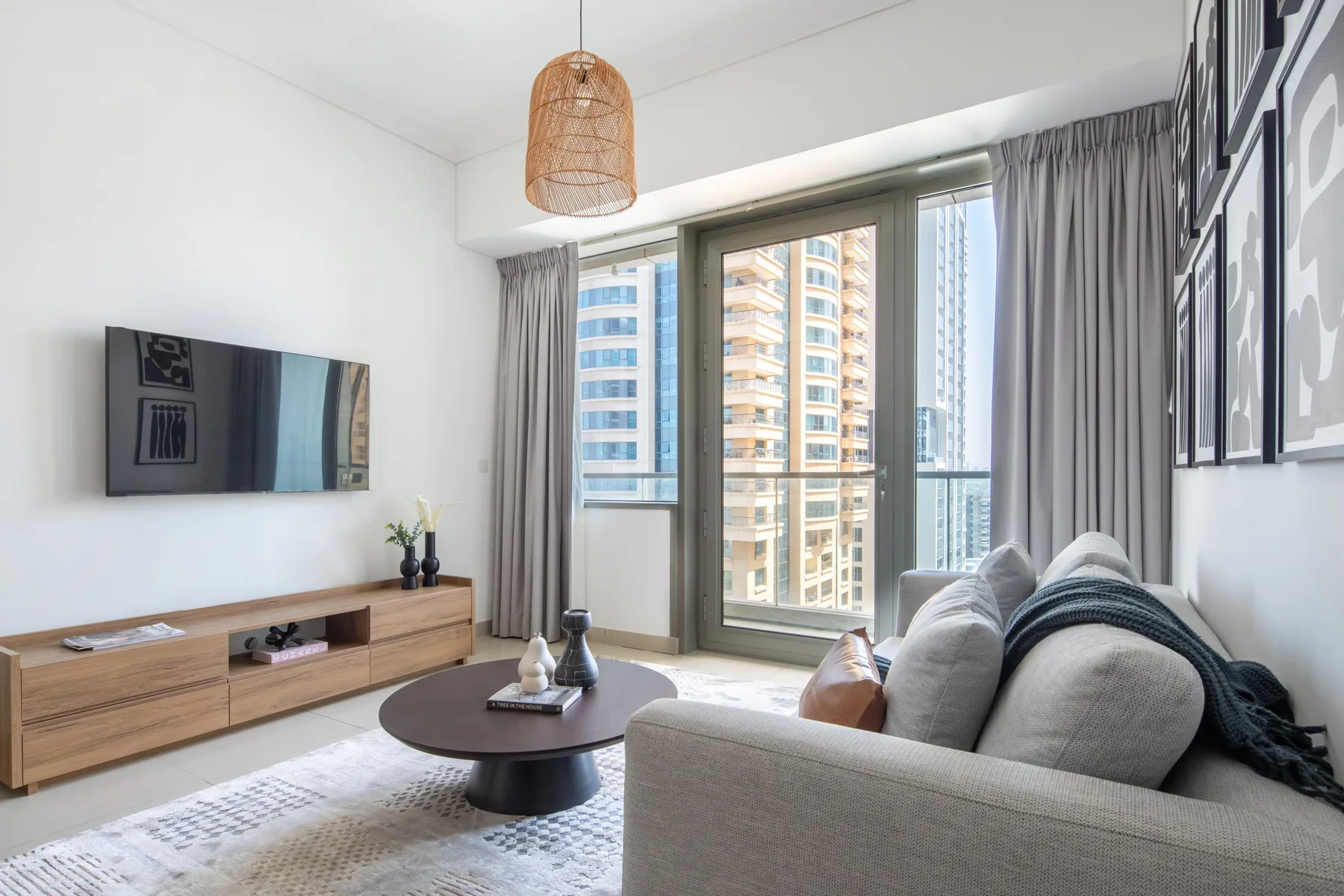 Una sala luminosa con televisor, asientos y grandes ventanas con vista a edificios cercanos.