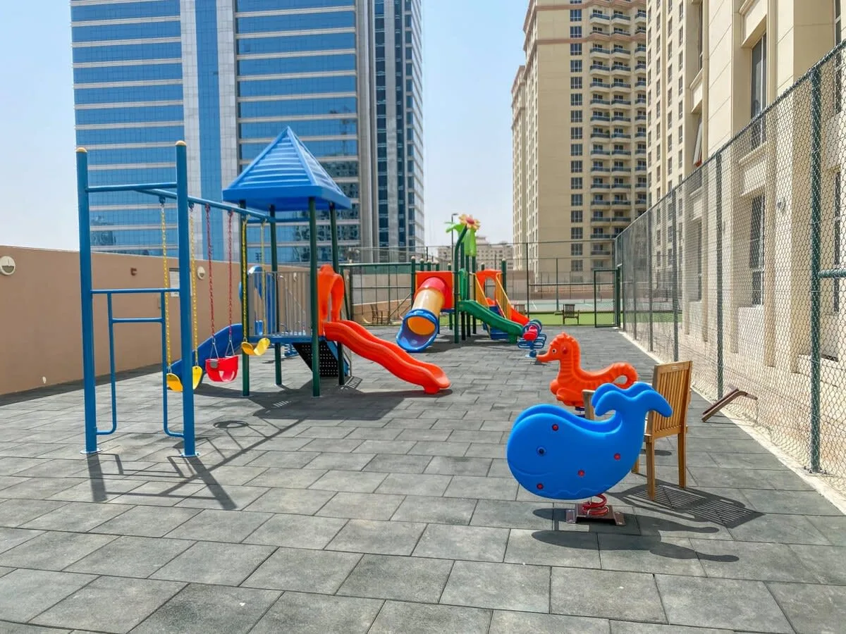Un parque infantil al aire libre con toboganes coloridos y juegos de muelle sobre una superficie pavimentada.