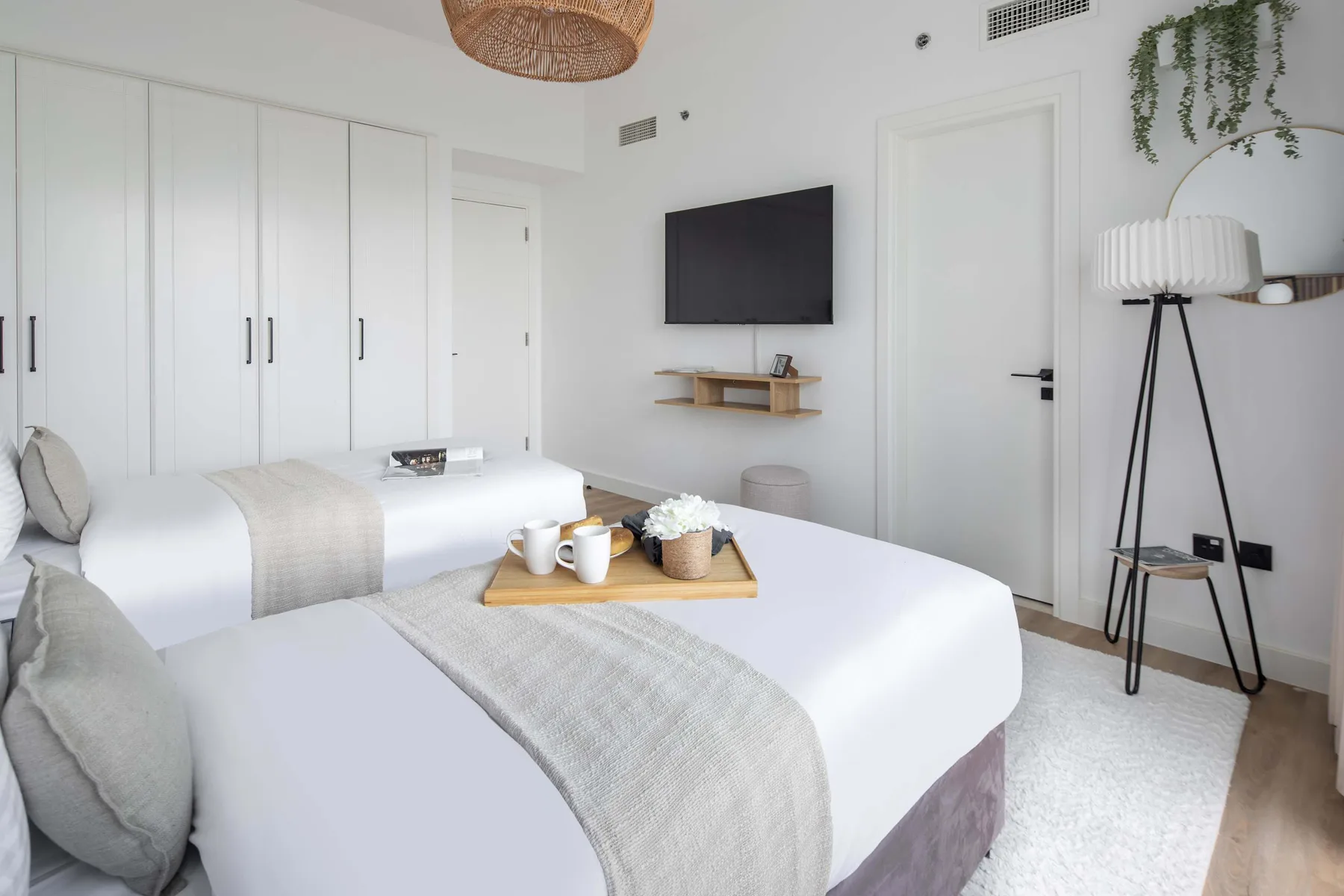 Un dormitorio luminoso con dos camas, ropa de cama blanca y un televisor en la pared.