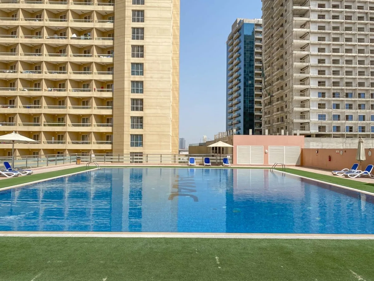 Una piscina al aire libre está entre edificios altos, con tumbonas cerca.