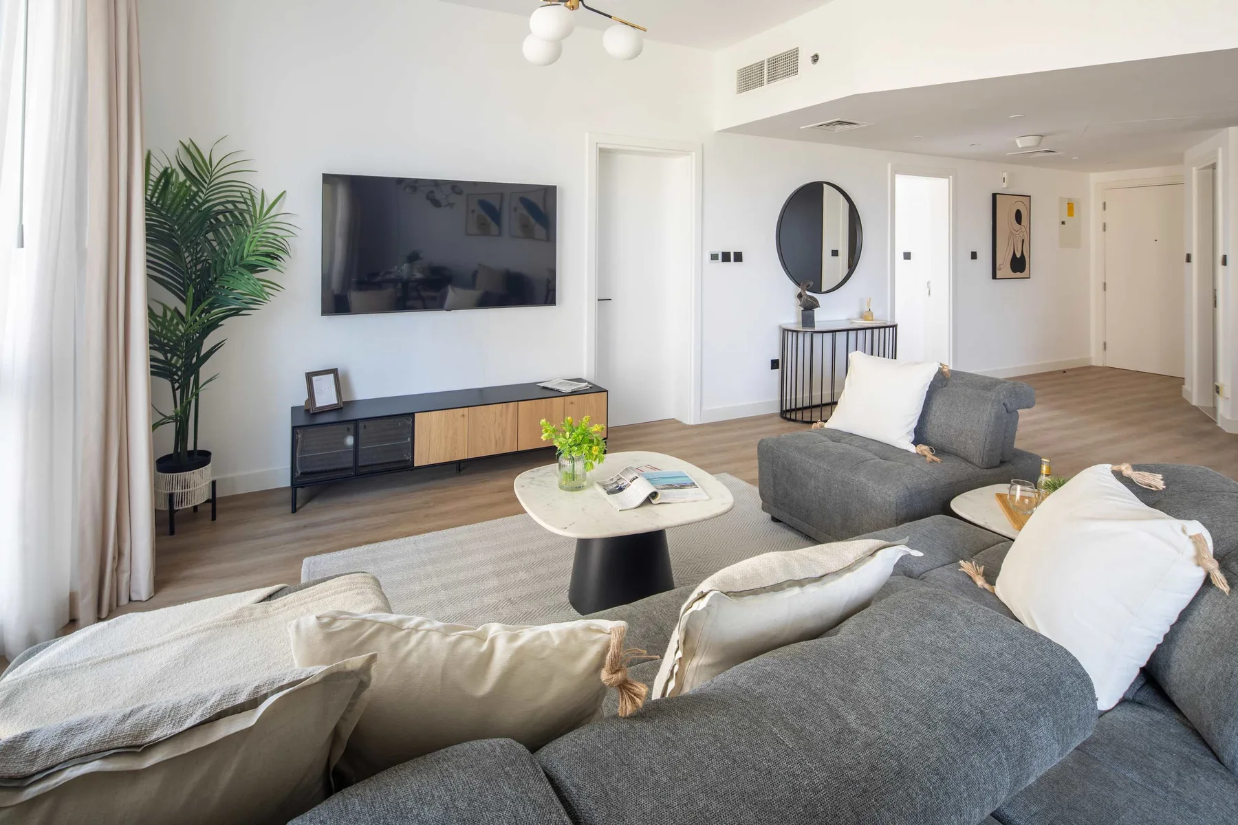 A bright living room with gray seating, a wall-mounted television, and a potted plant.
