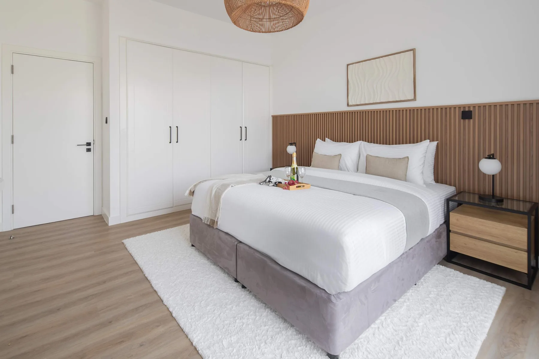 Un dormitorio luminoso cuenta con una cama grande, ropa de cama blanca y un cabecero revestido de madera.