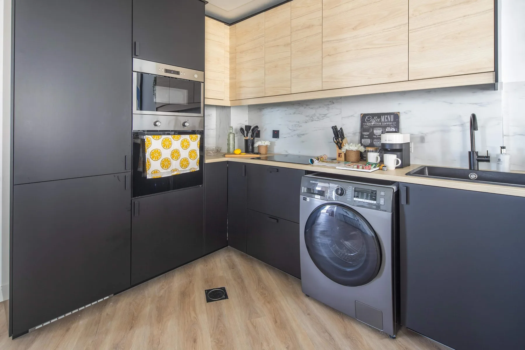 Una cocina moderna con armarios oscuros, gabinetes de madera clara y una lavadora.