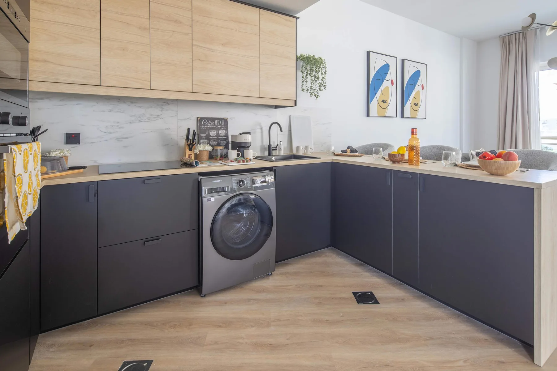 Una cocina moderna con armarios inferiores oscuros, gabinetes de madera clara y una lavadora.