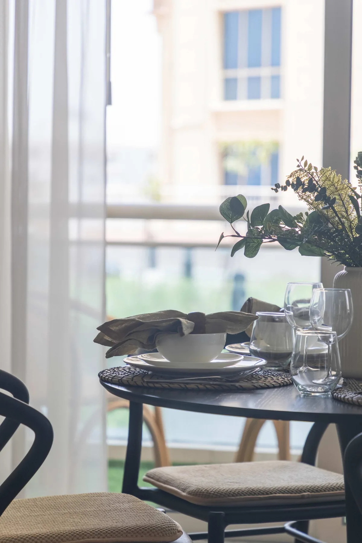 Una mesa de comedor con platos está junto a una ventana grande.