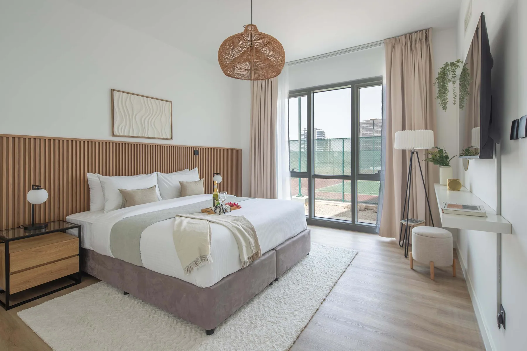 Un dormitorio luminoso con una cama, mesitas de noche y grandes puertas de vidrio.