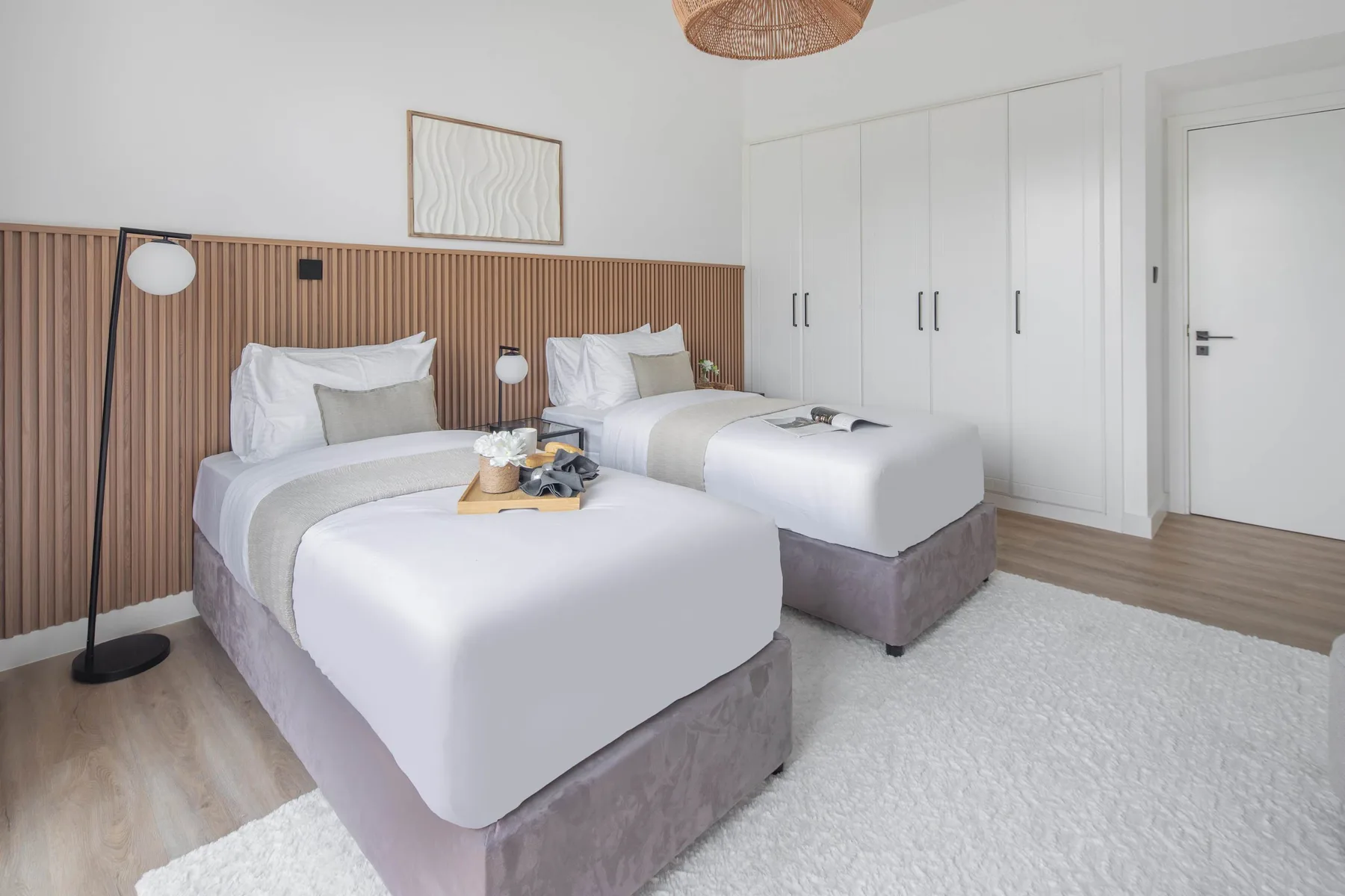 Un dormitorio luminoso con dos camas bien tendidas y un cabecero de paneles de madera.