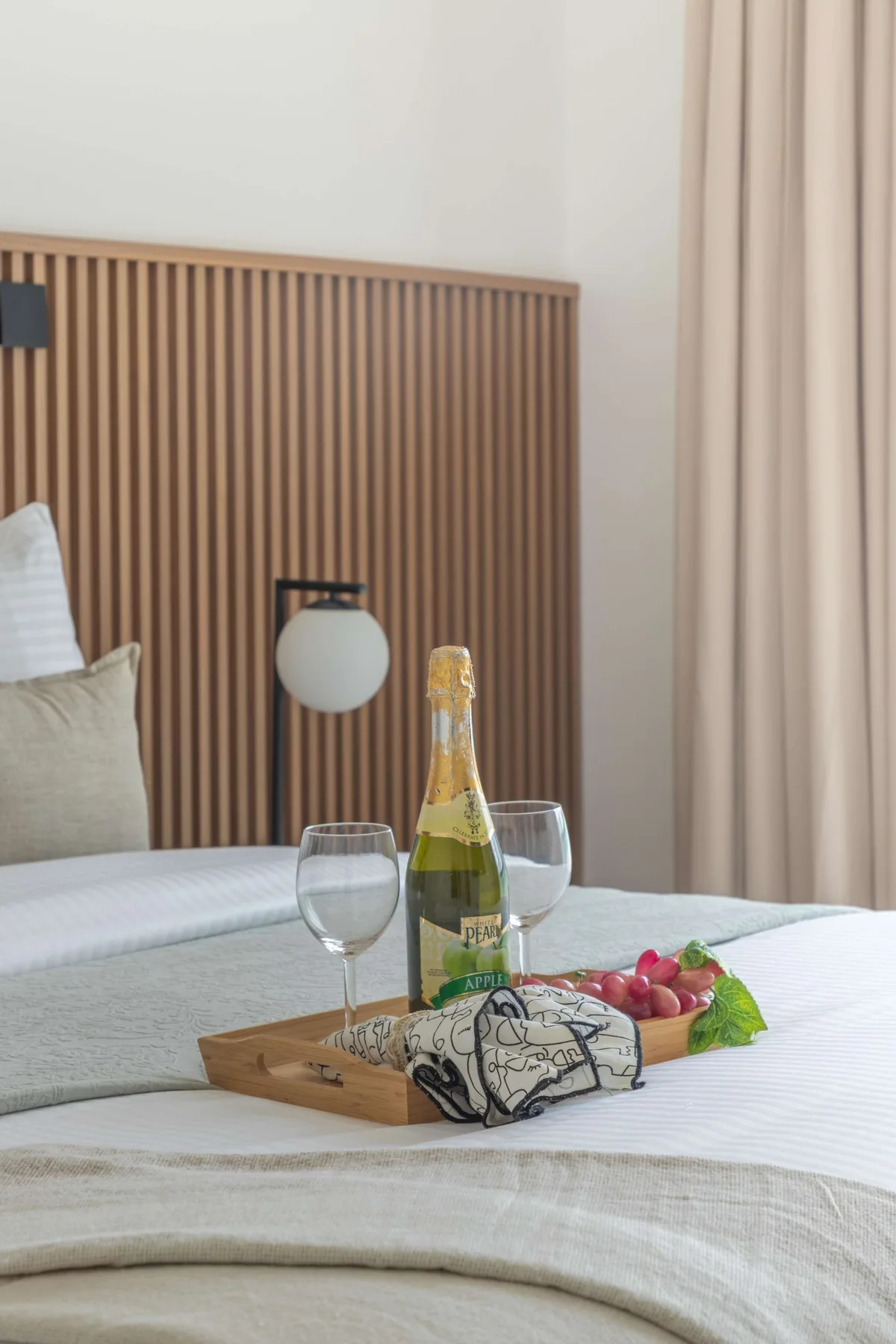 Un dormitorio con una cama bien tendida y una bandeja con bebidas y fruta.