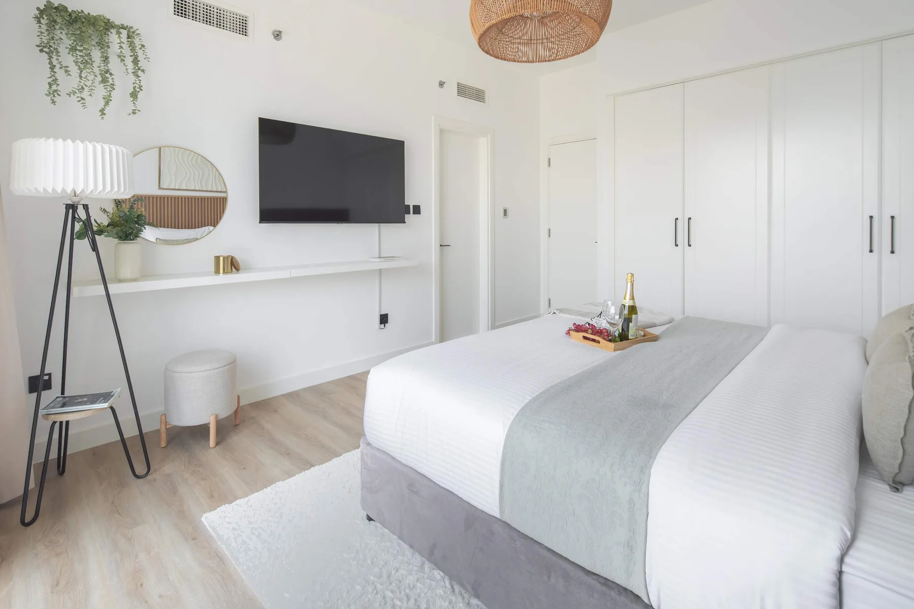 Un dormitorio luminoso con una cama bien arreglada y un televisor en la pared.