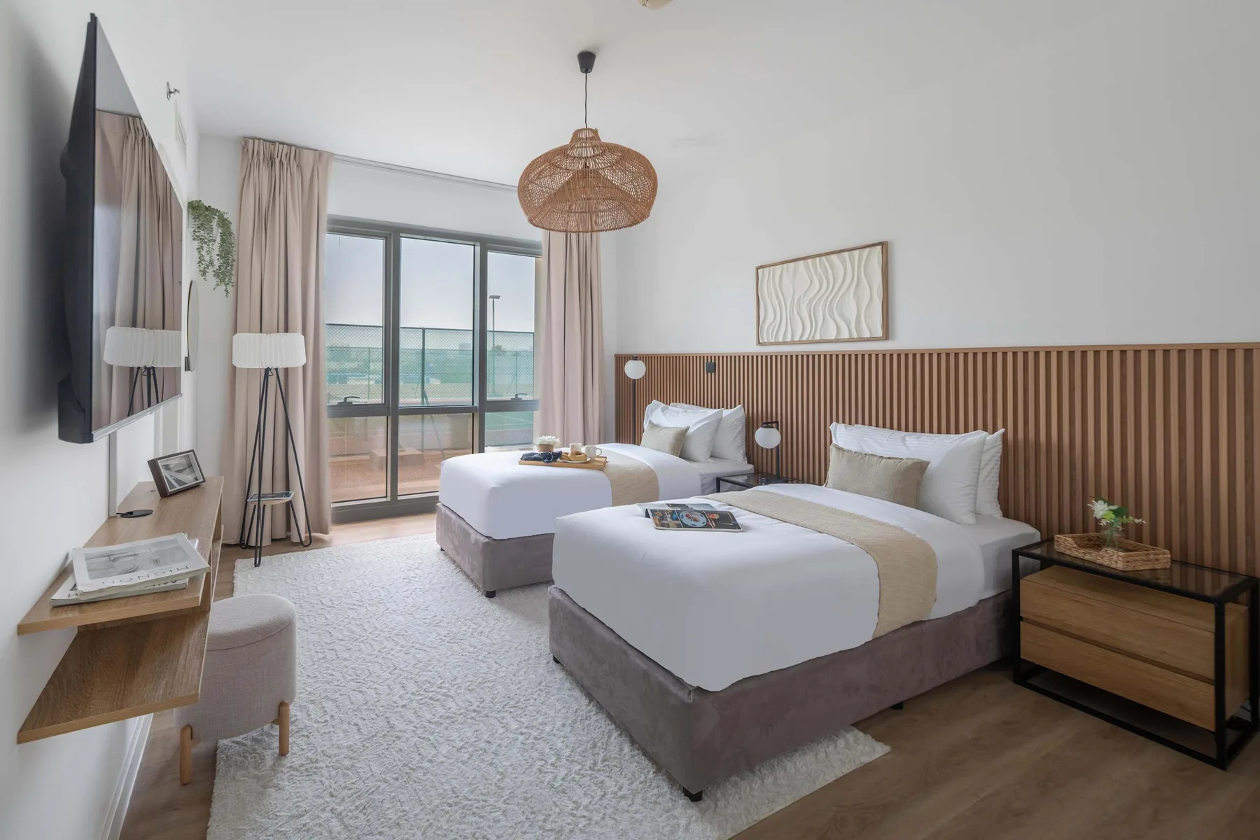 Un dormitorio luminoso con dos camas, una ventana grande y una lámpara colgante tejida.