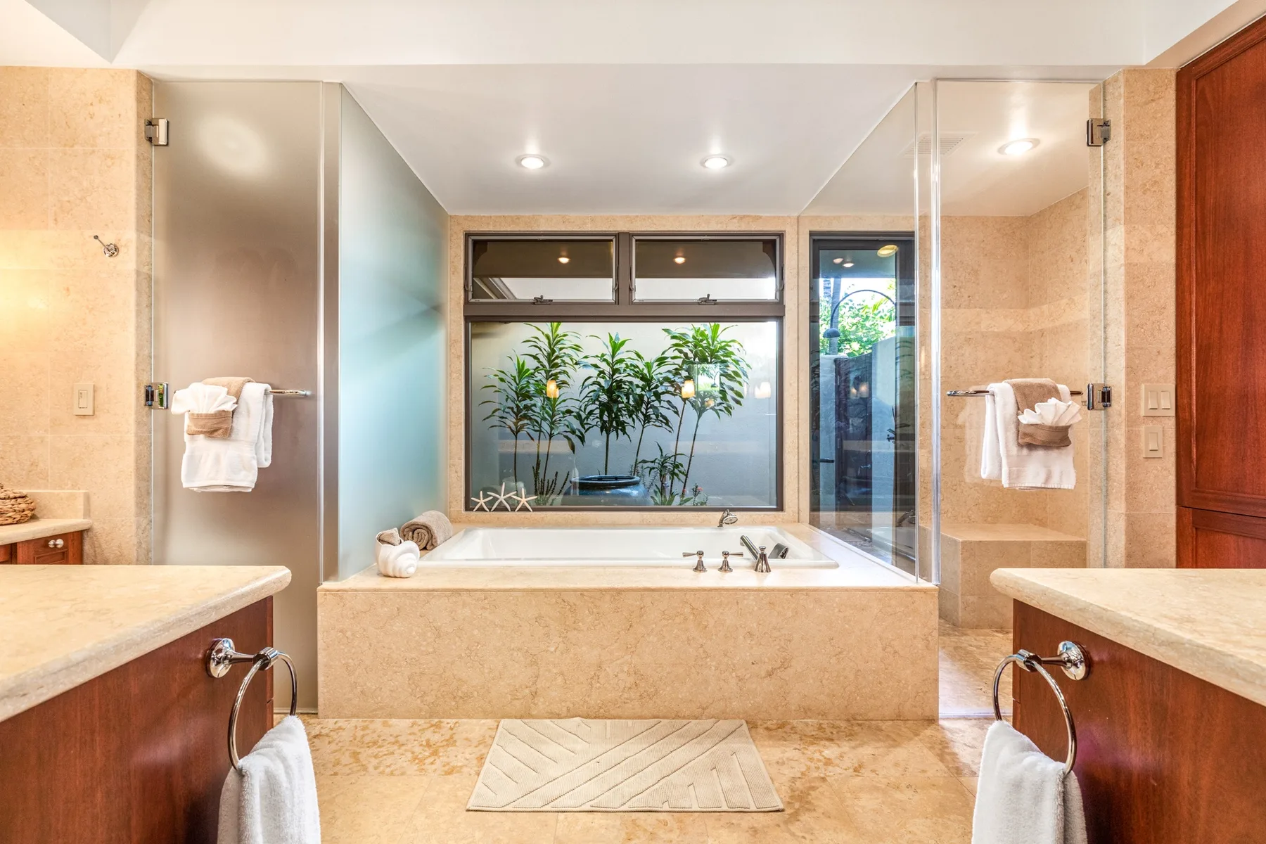 A spacious bathroom features a built-in bathtub beneath a wide window overlooking greenery.