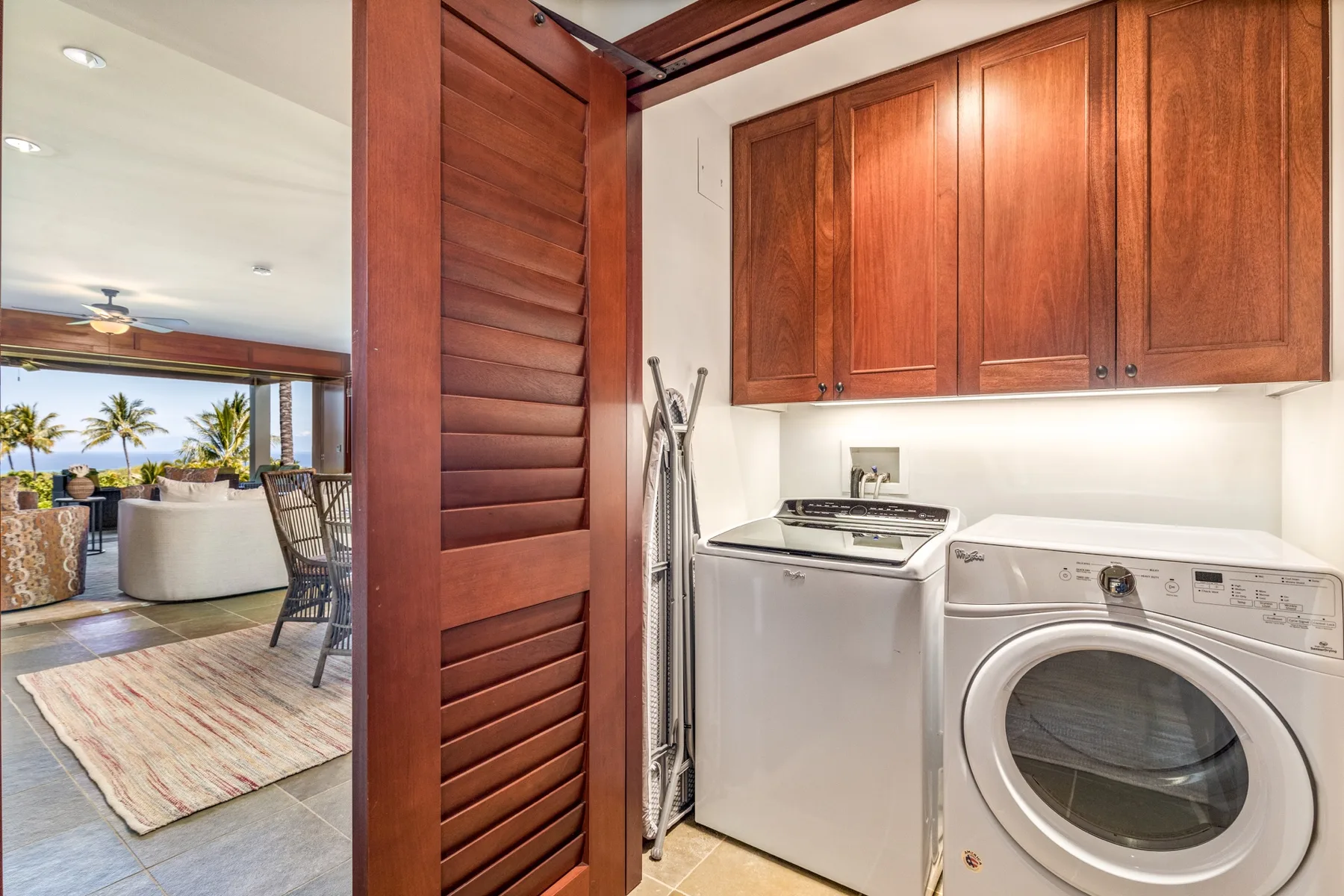 A laundry area with a washer, dryer, and wooden cabinets beside an open living space.