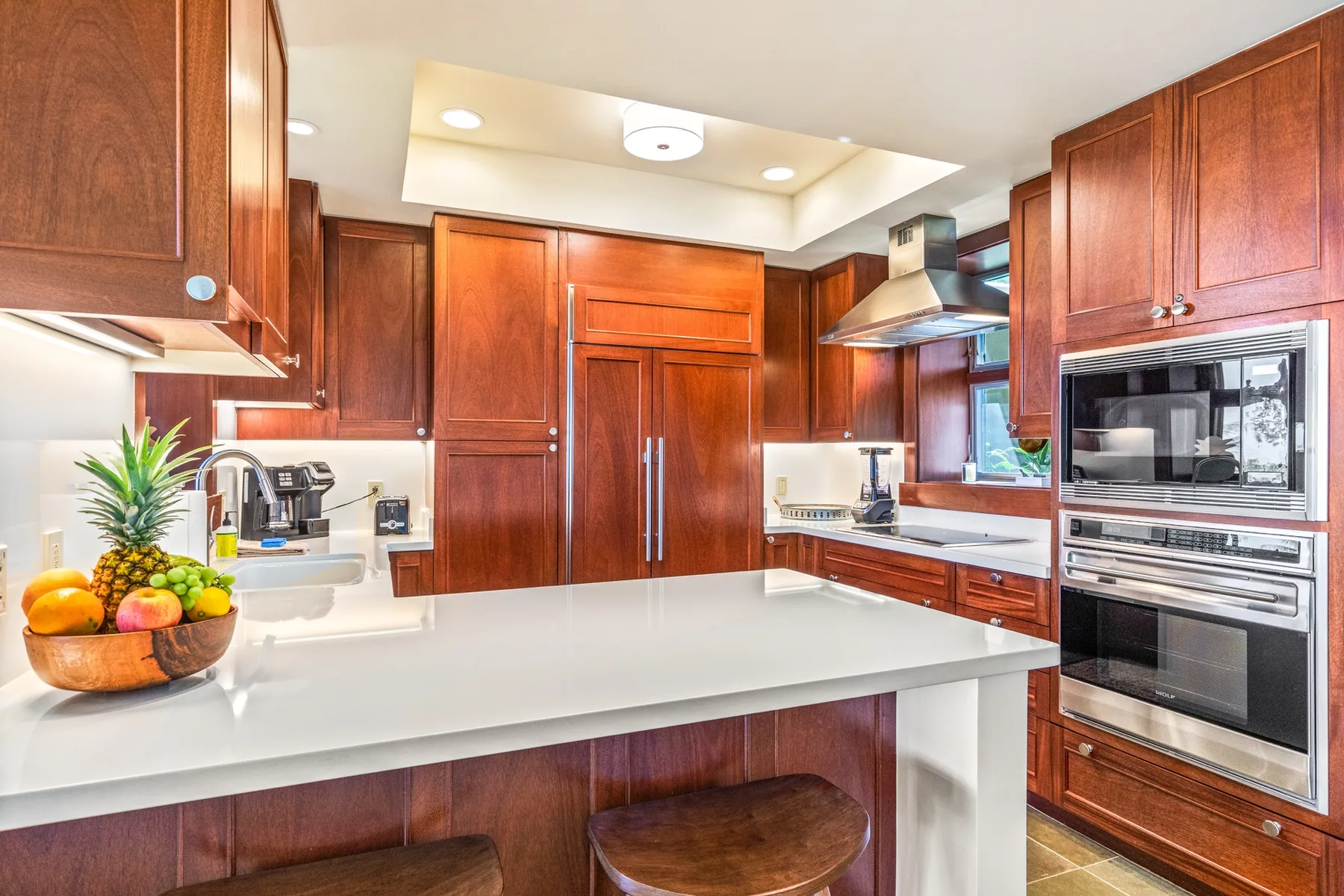 A kitchen with reddish wood cabinets, white countertops, and built-in appliances.