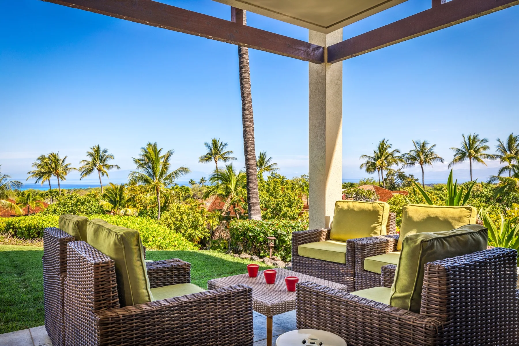 An outdoor patio seating area overlooks palm trees and the ocean.