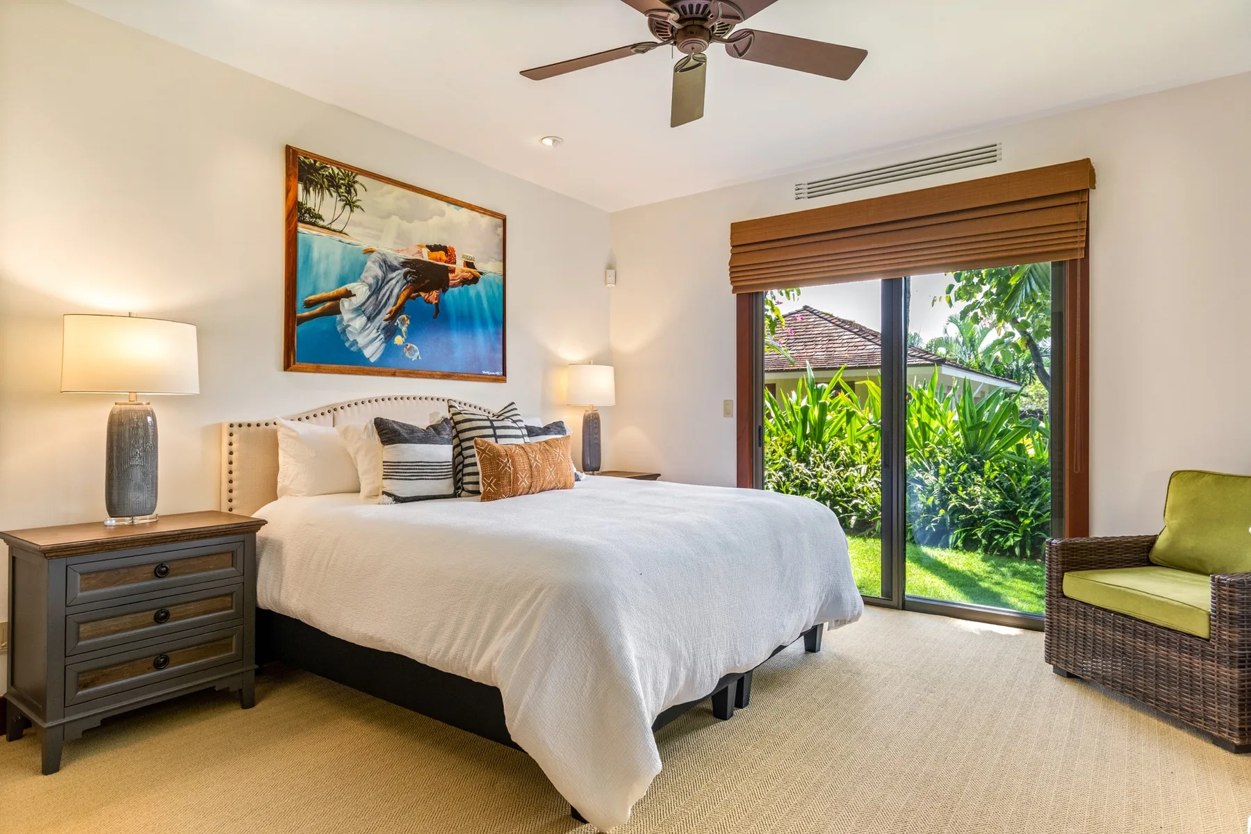 A bedroom with a neatly made bed and sliding glass doors opening onto greenery.