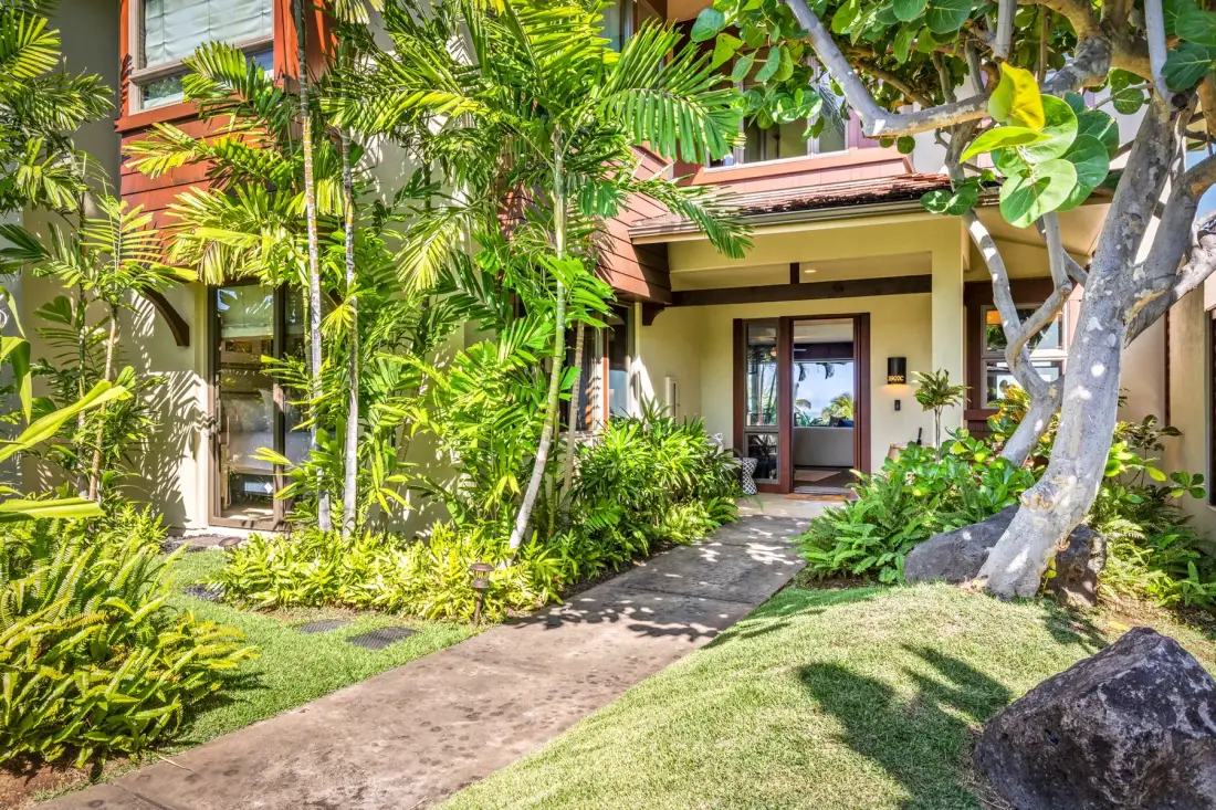 A garden path leads through lush tropical plants to a house entrance.