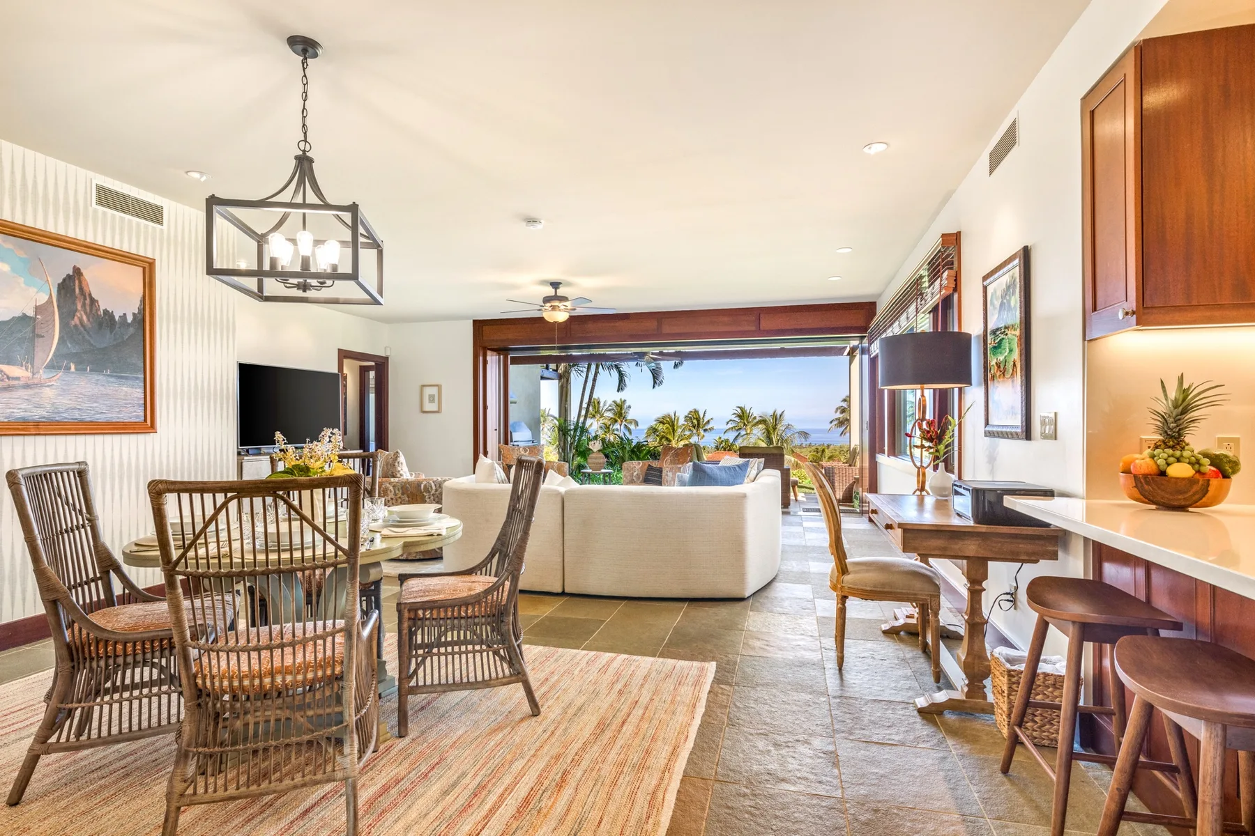An open-plan living and dining room faces large windows overlooking greenery and water.