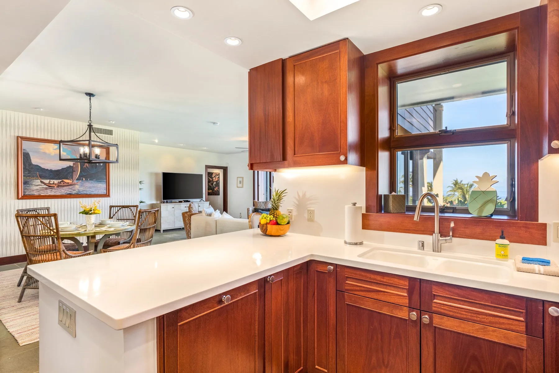 A bright kitchen with wooden cabinets, a white island, and a sink beneath a large window.