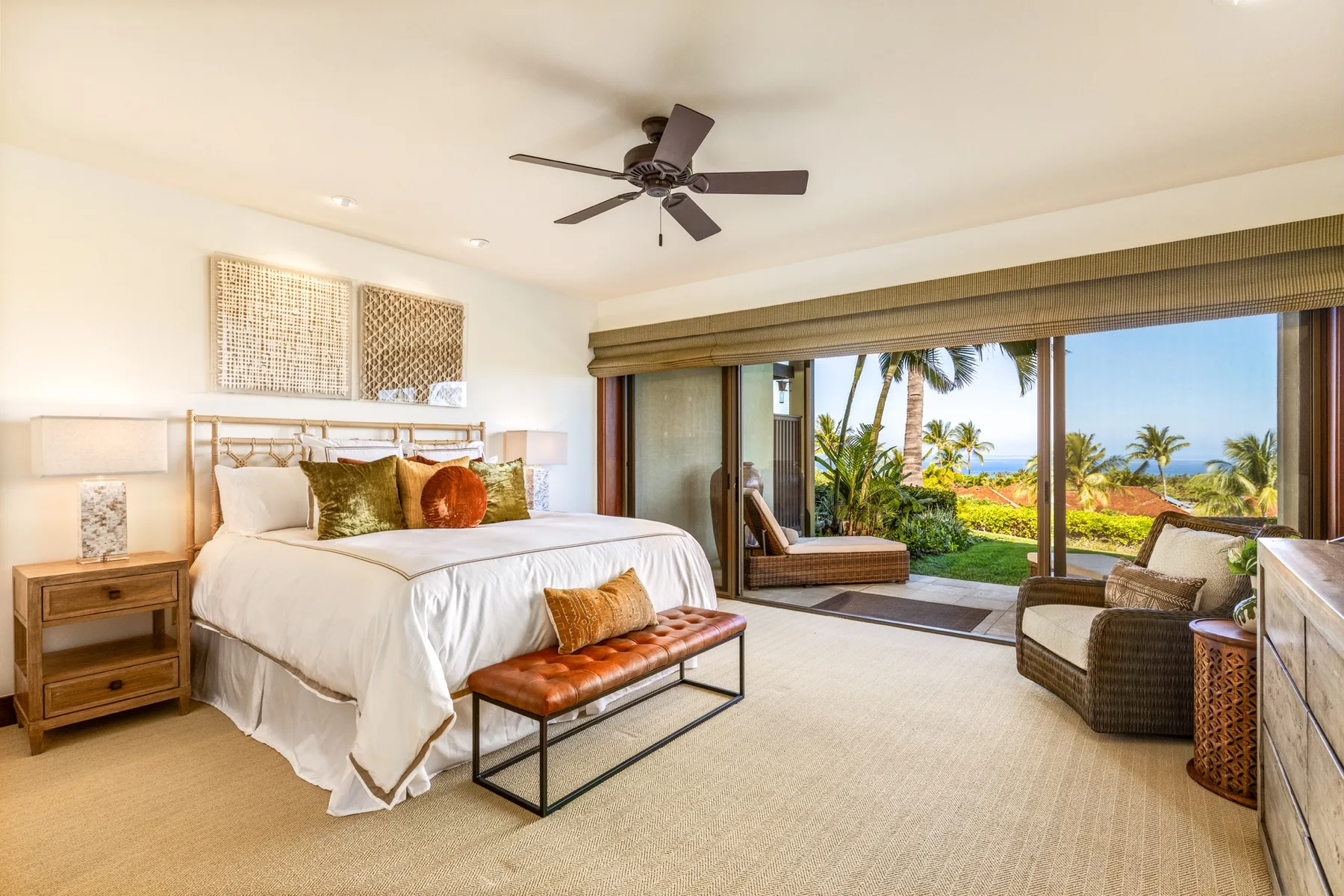 A bright bedroom opens onto a furnished patio with tropical greenery and ocean views.