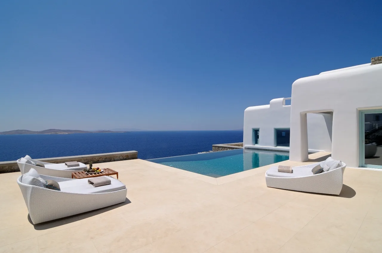 A seaside terrace with a swimming pool and white outdoor seating.