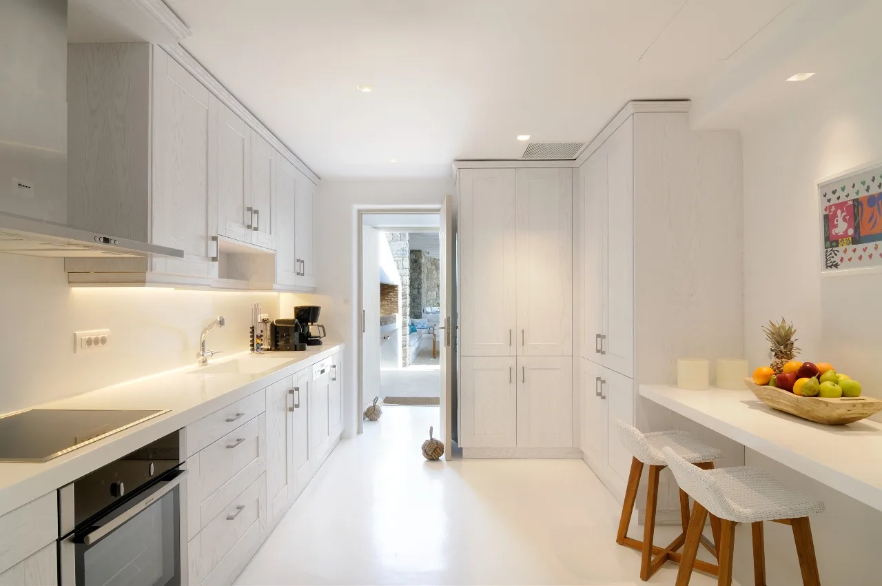A bright white kitchen with a long counter and a small dining area.