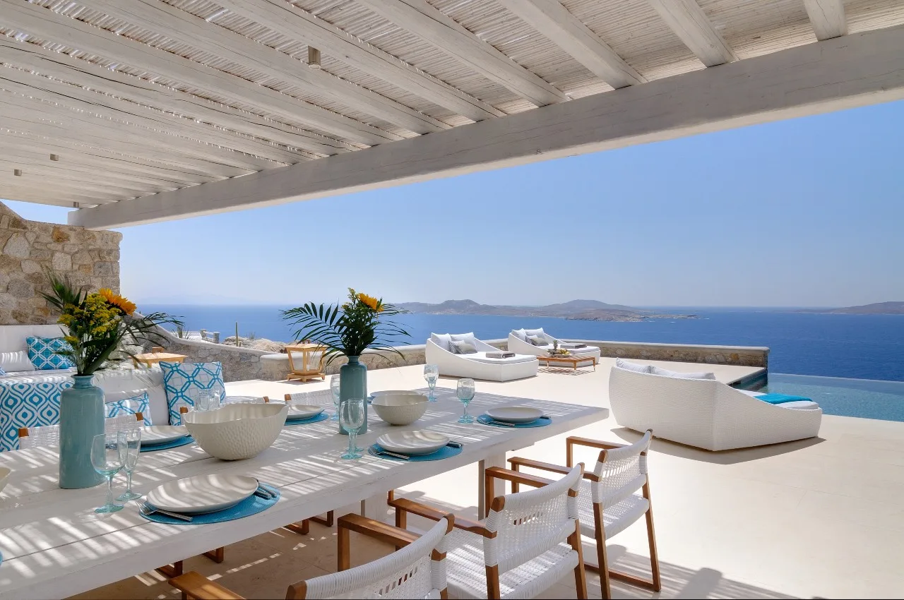 A shaded outdoor dining area overlooks the sea, with a table and lounge seating.