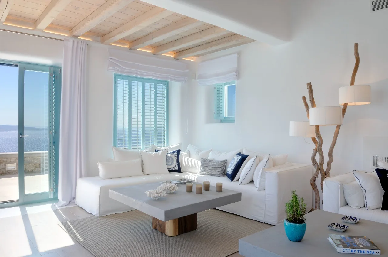 A bright living room with white seating and large windows opening onto a balcony.